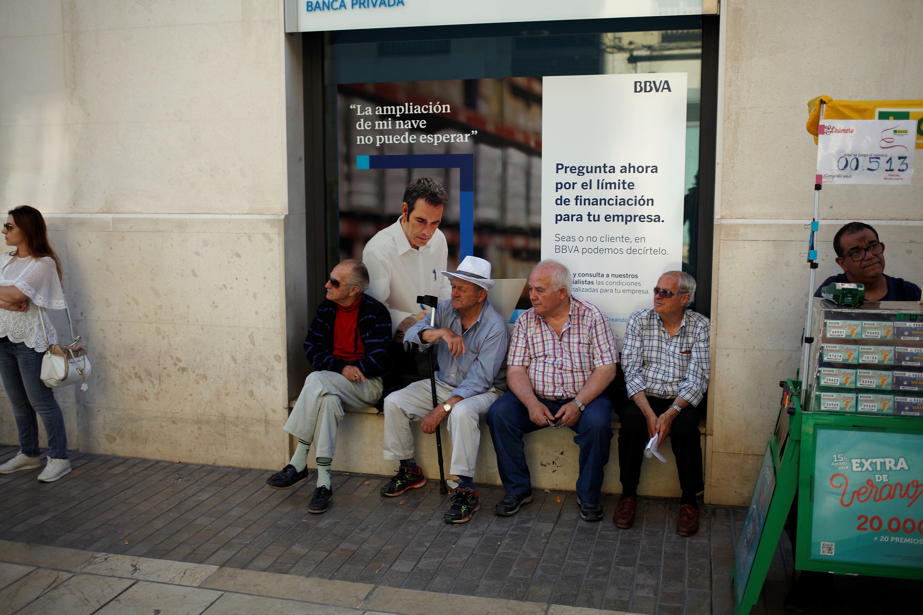 Pensionistas sentados enfrente de una sede del BBVA.