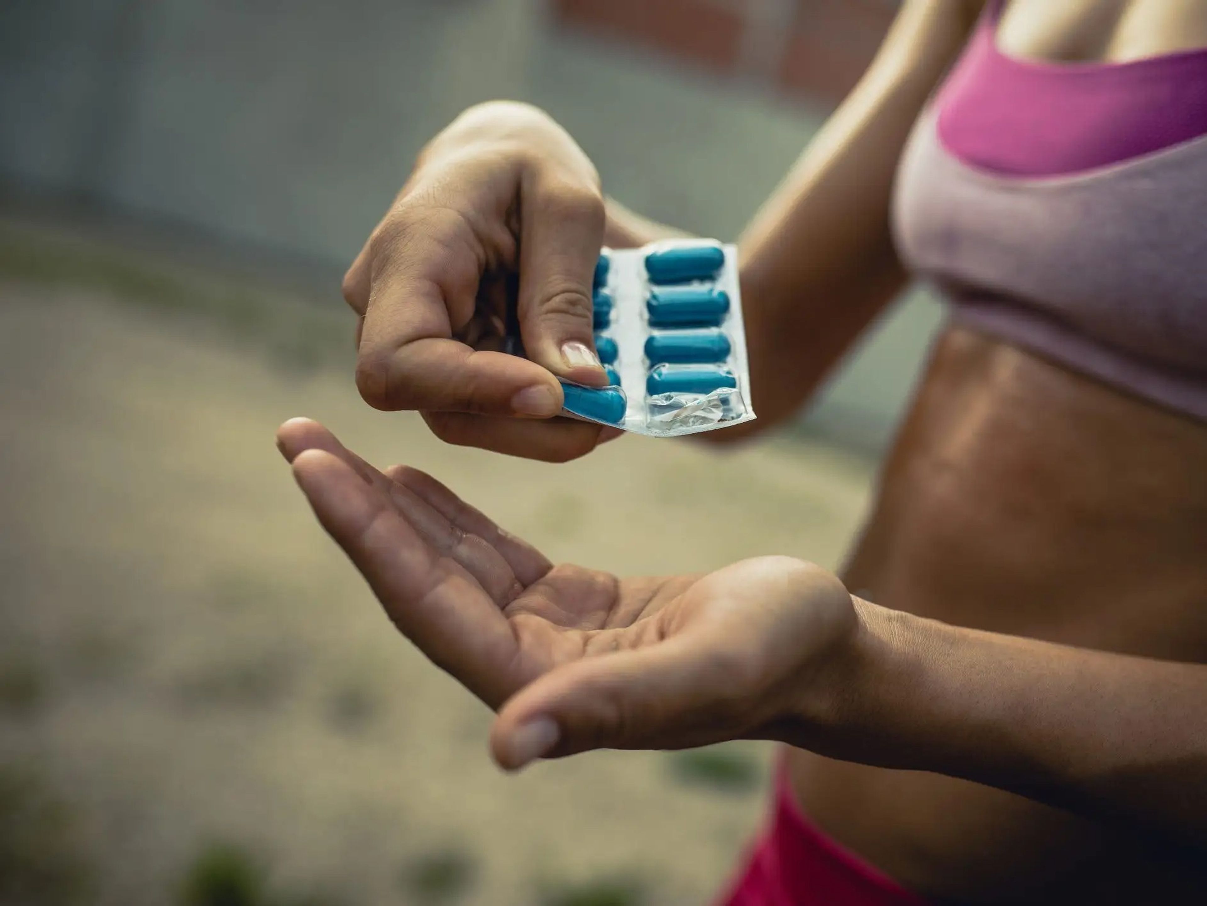 close-up image of a person in a sports bra taking supplement pills