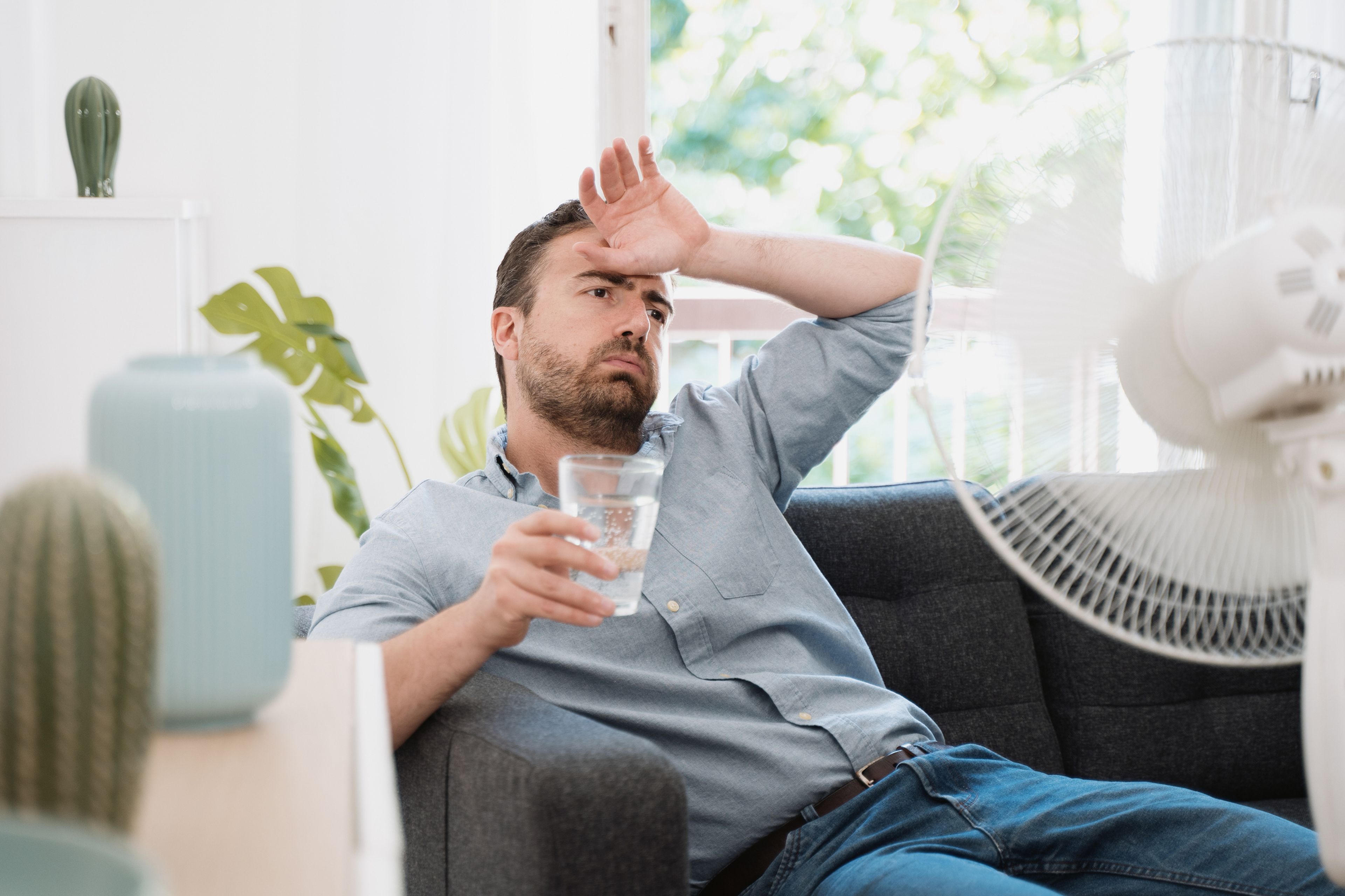 Un hombre trata de refrescarse con un vaso de agua y un ventilador.