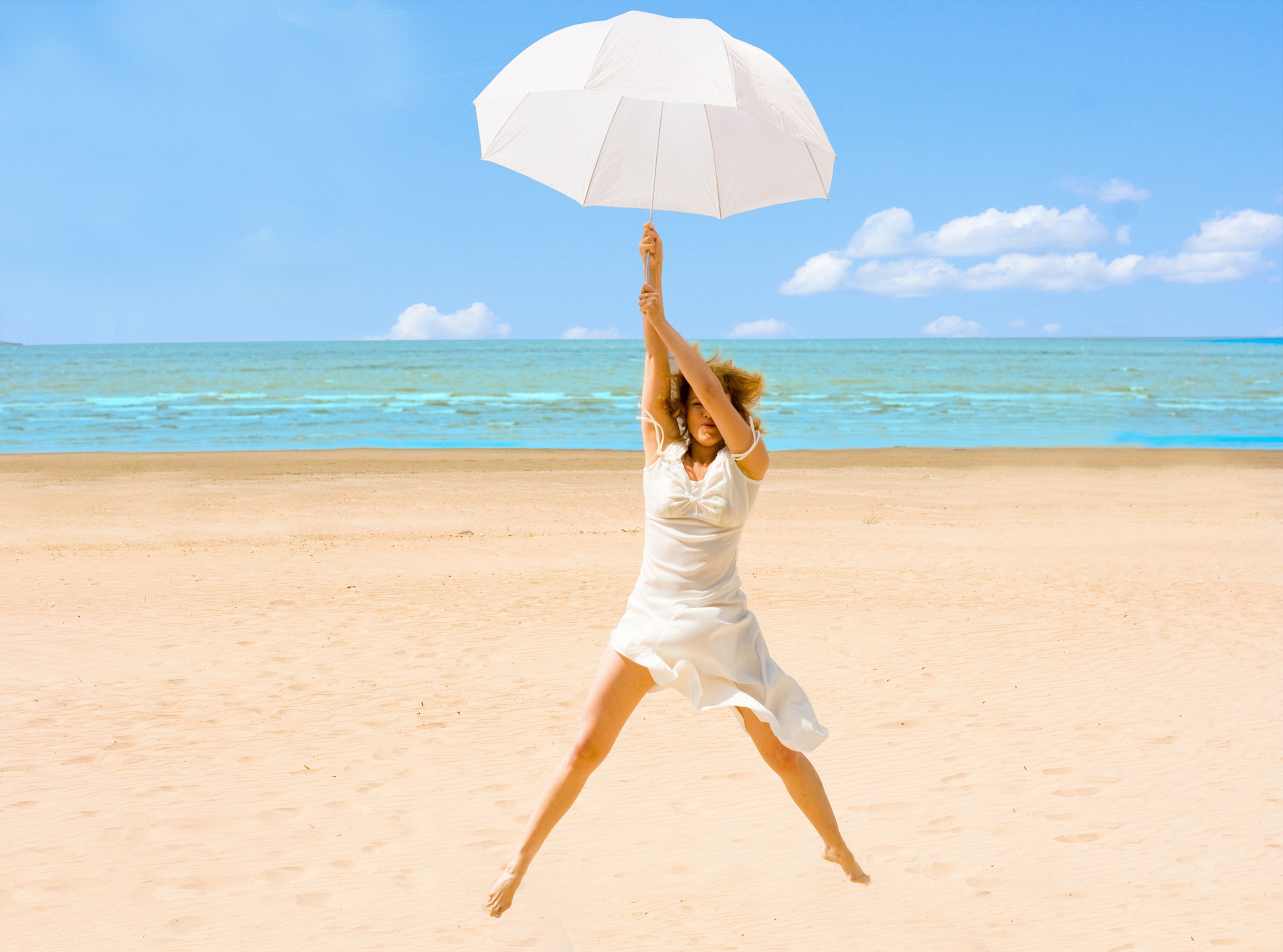 Una mujer sale volando agarrada a un paraguas en la playa.