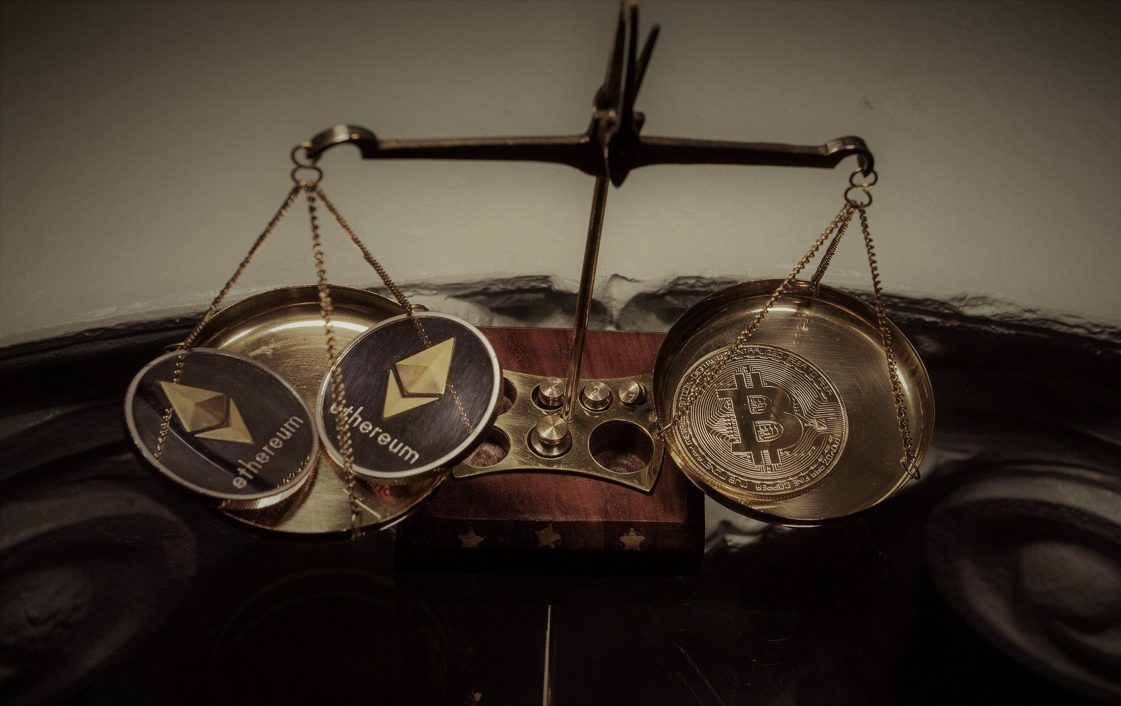 2 monedas de ethereum y una de bitcoin en una balanza.