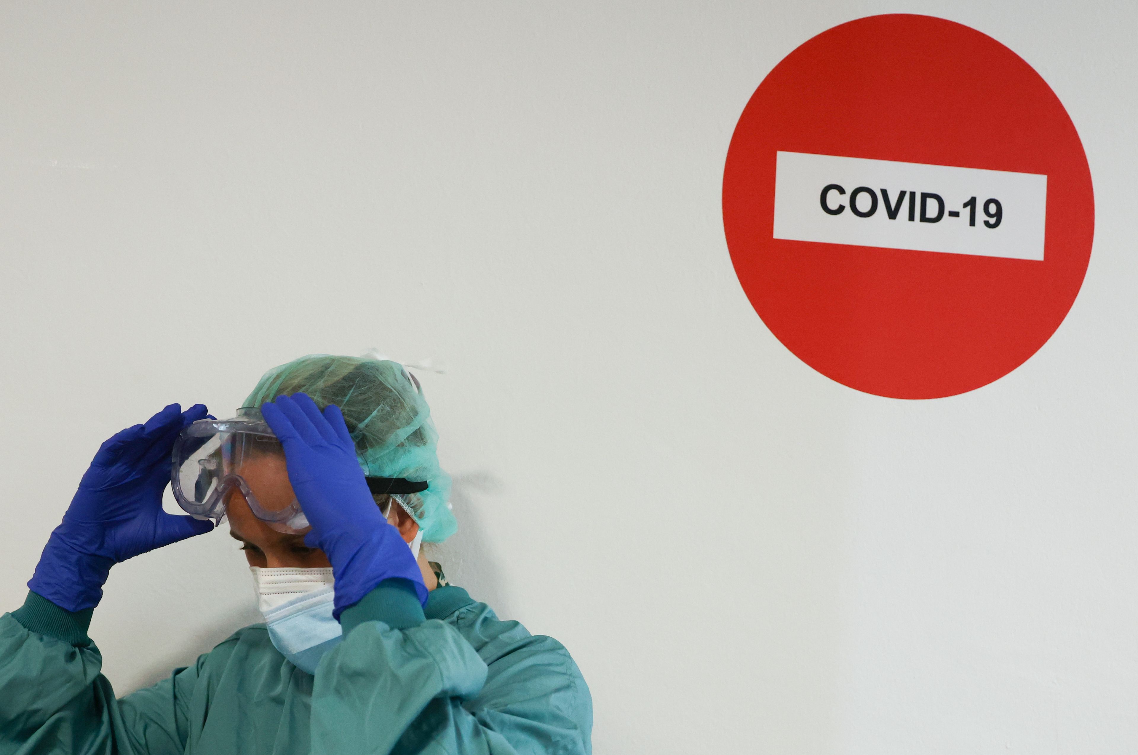 Un médico poniéndose las gafas de protección junto a un cartel de prohibido COVID-19