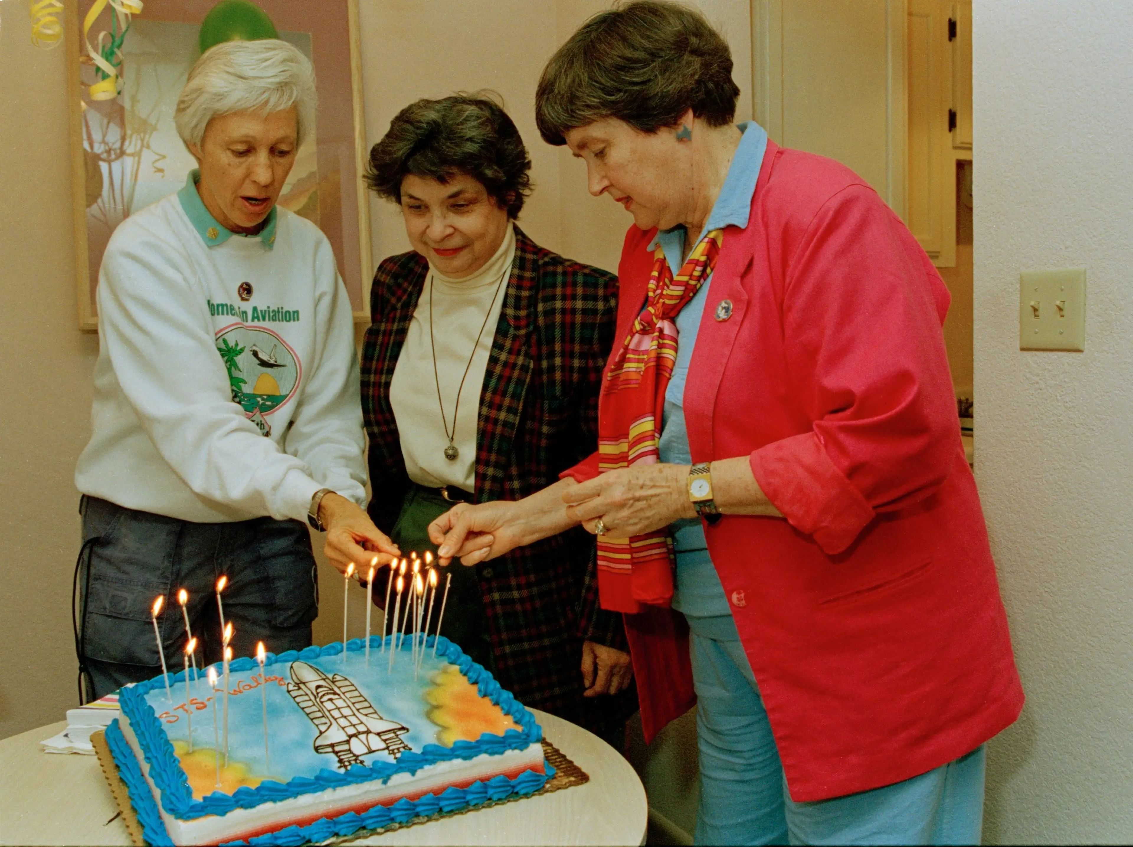 Wally Funk and two other women from Mercury 13 stand over a birthday cake with candles