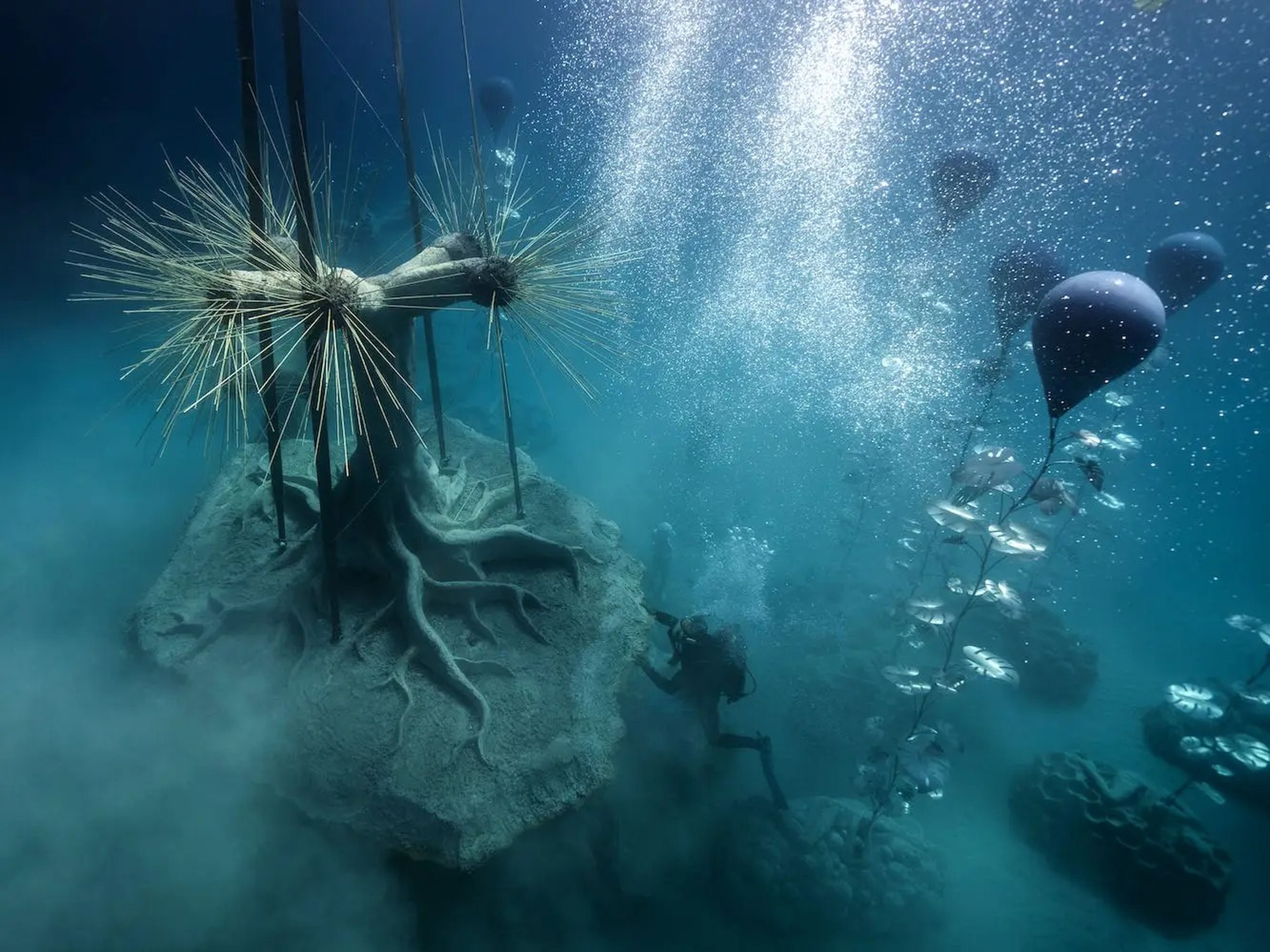 Una grúa baja una escultura al fondo del océano.