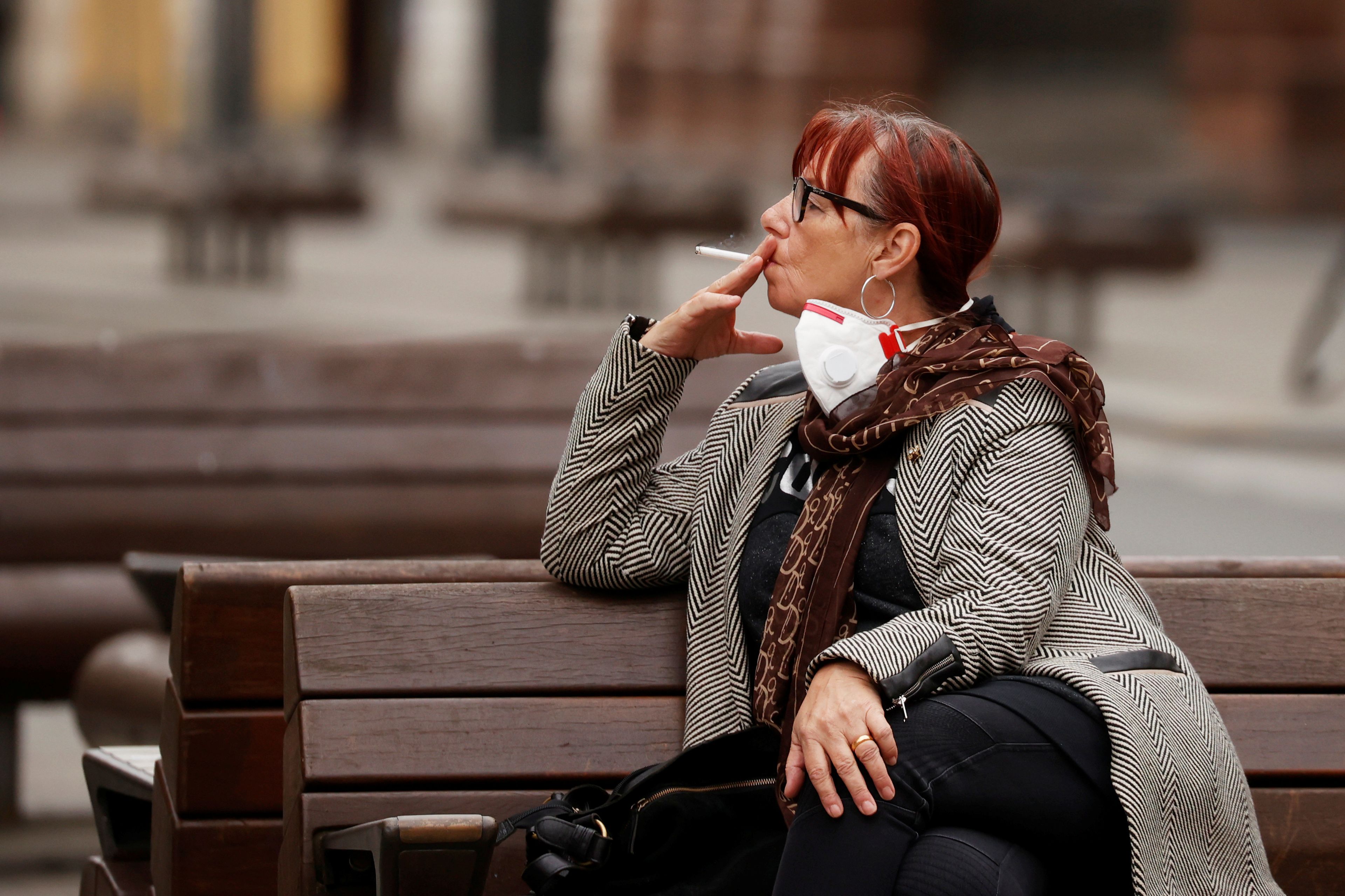Una mujer fuma sentada en un banco