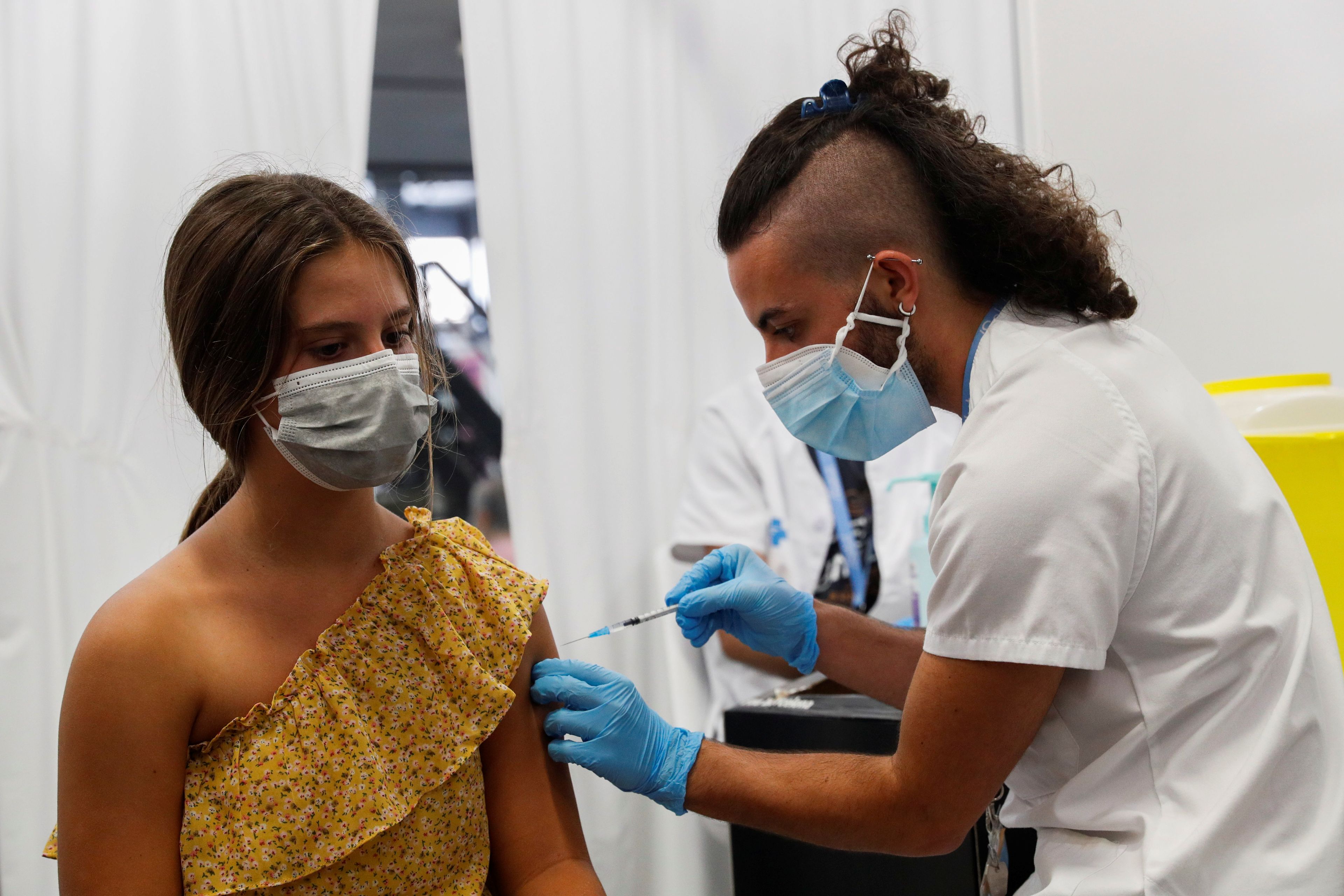 Un sanitario pone una dosis de la vacuna contra el COVID-19 a una menor en Barcelona