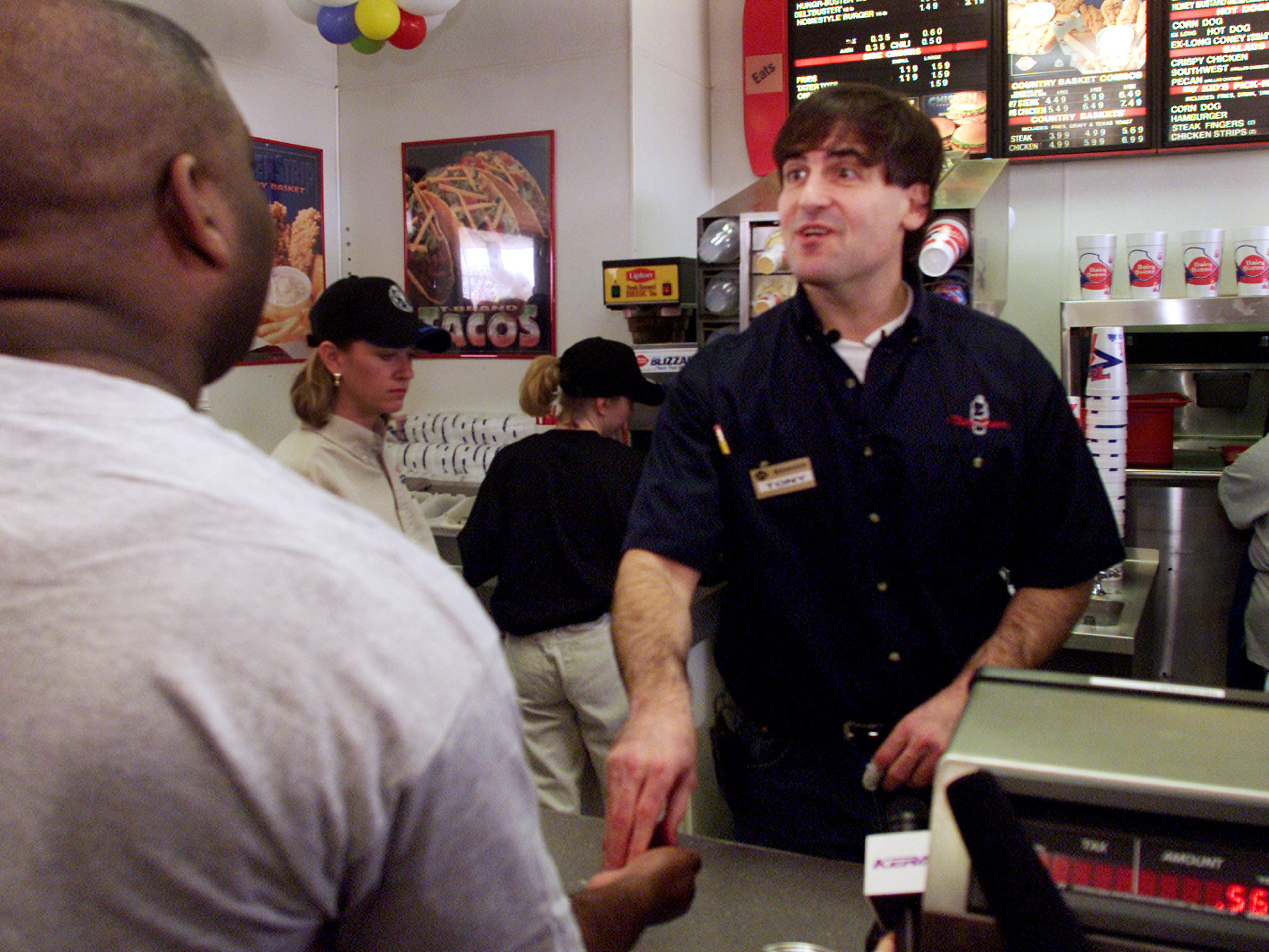 Mark Cuban le entrega el cambio a un cliente mientras trabaja en el mostrador de una franquicia de comida rápida.