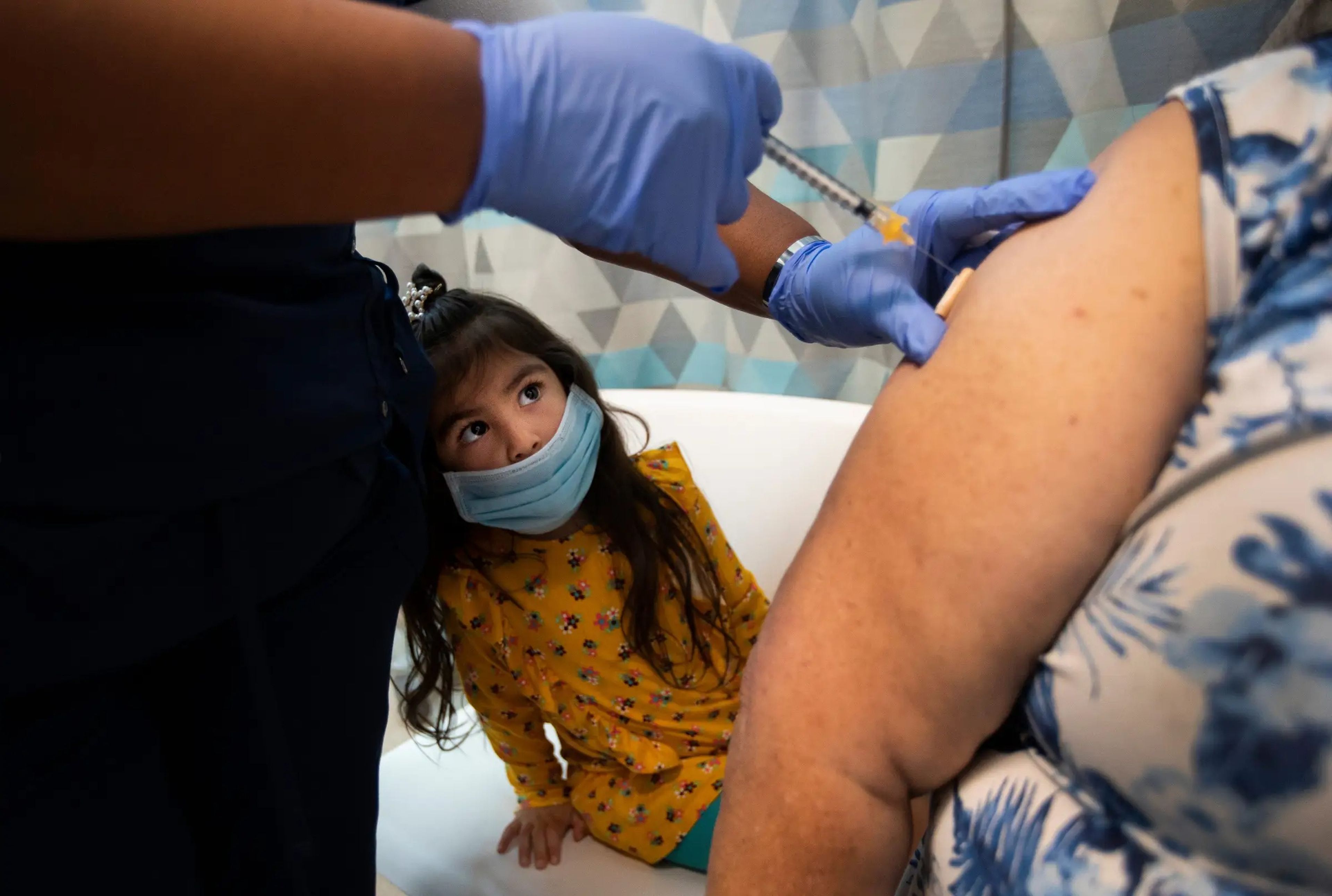 Una niña mira cómo vacunan a una mujer contra el COVID-19.