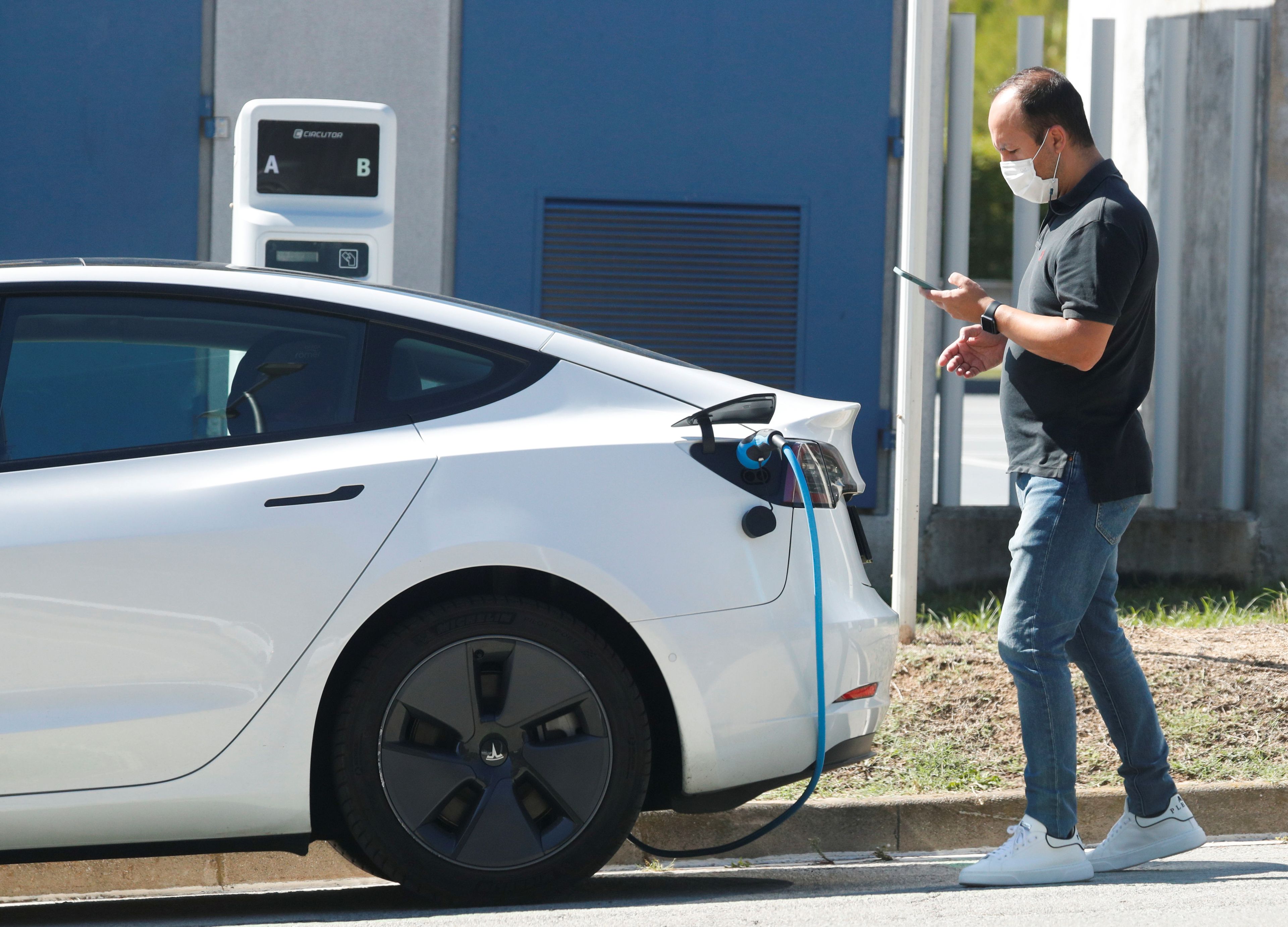 Un hombre mira su móvil mientras carga un coche eléctrico en Sant Cugat del Valles