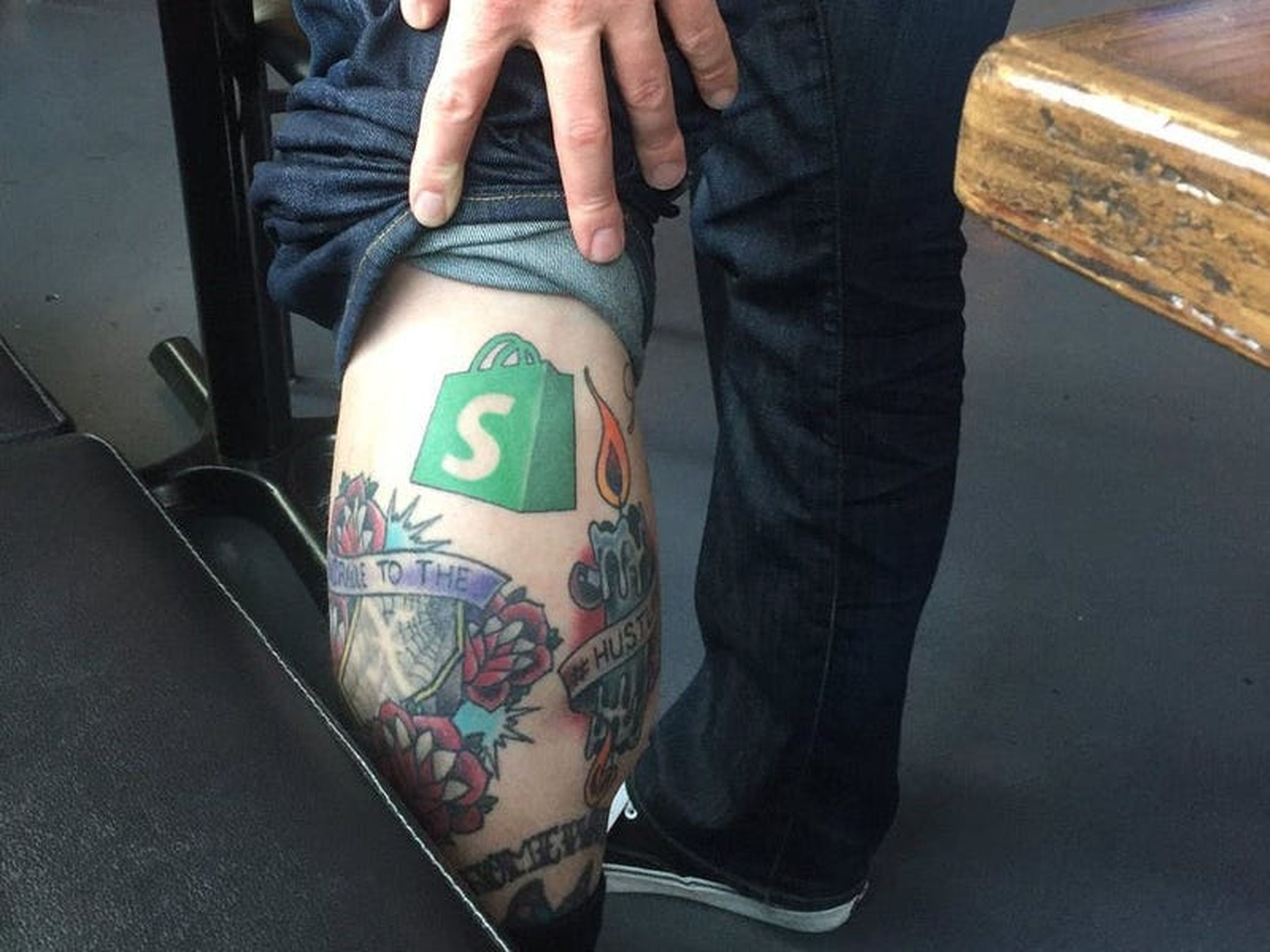 Josh Highland muestra el tatuaje del logo de Shopify que tiene en su pierna.