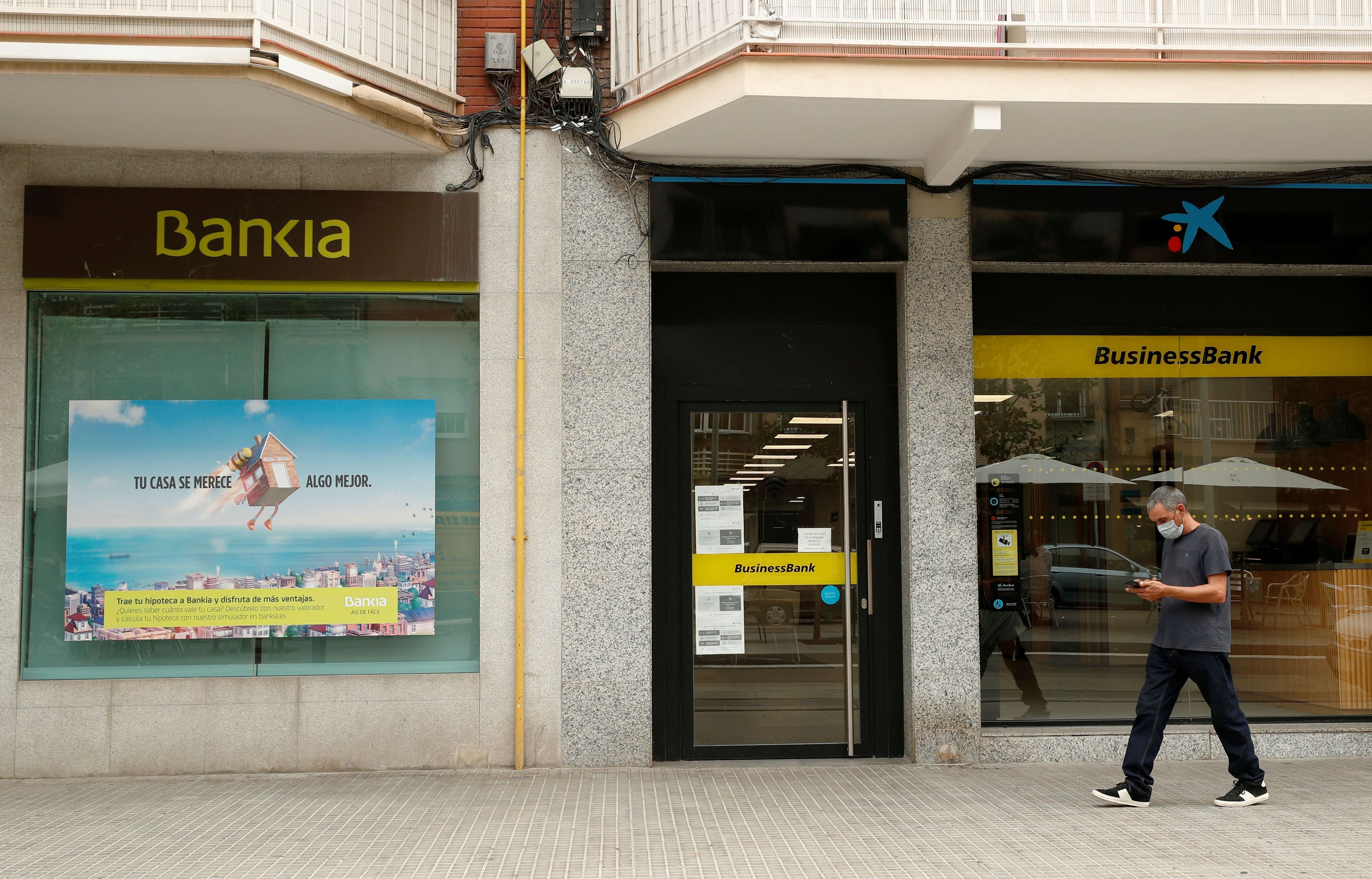 Un hombre pasa por unos cajeros de CaixaBank y Bankia