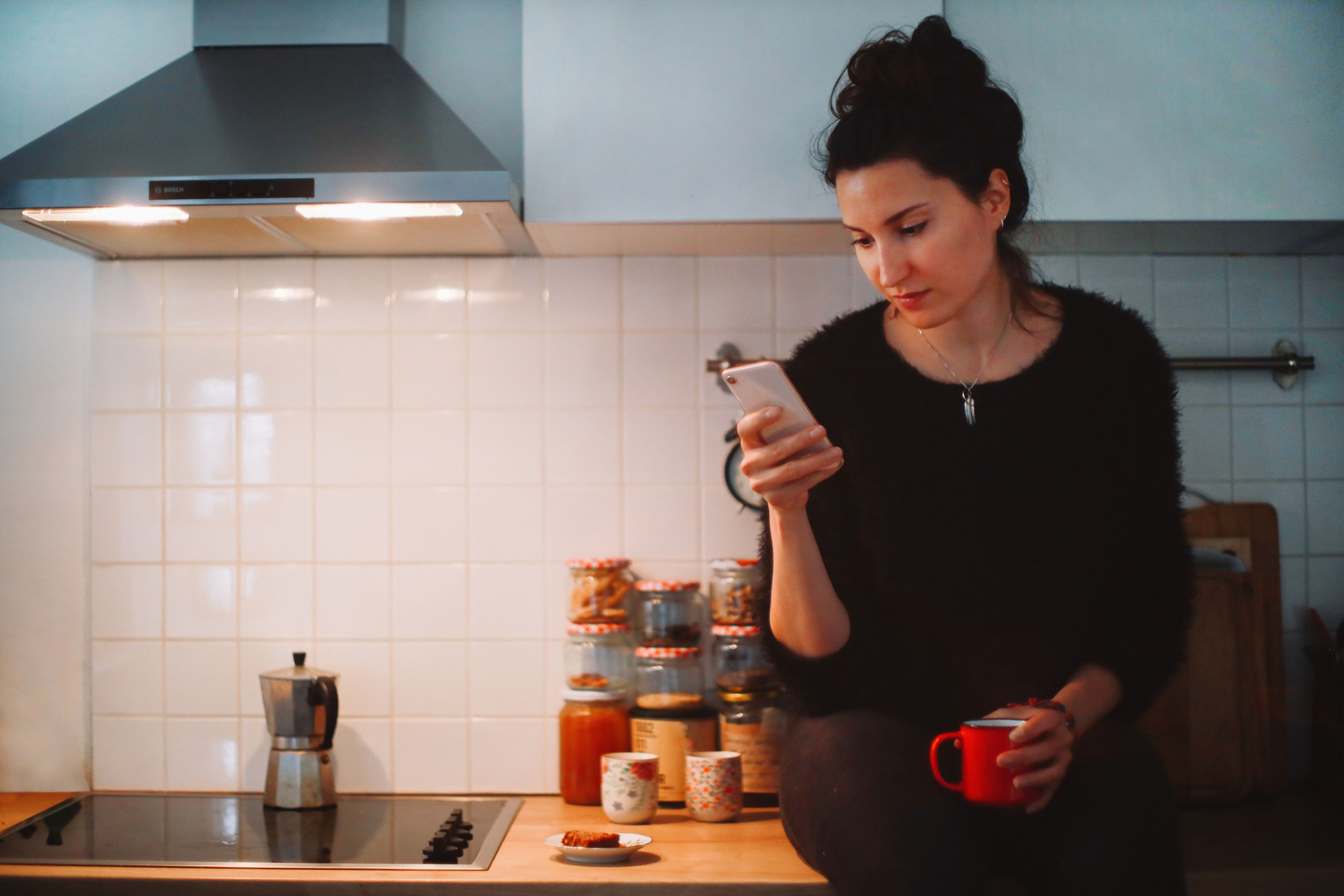 Una mujer mira su teléfono móvil en la cocina