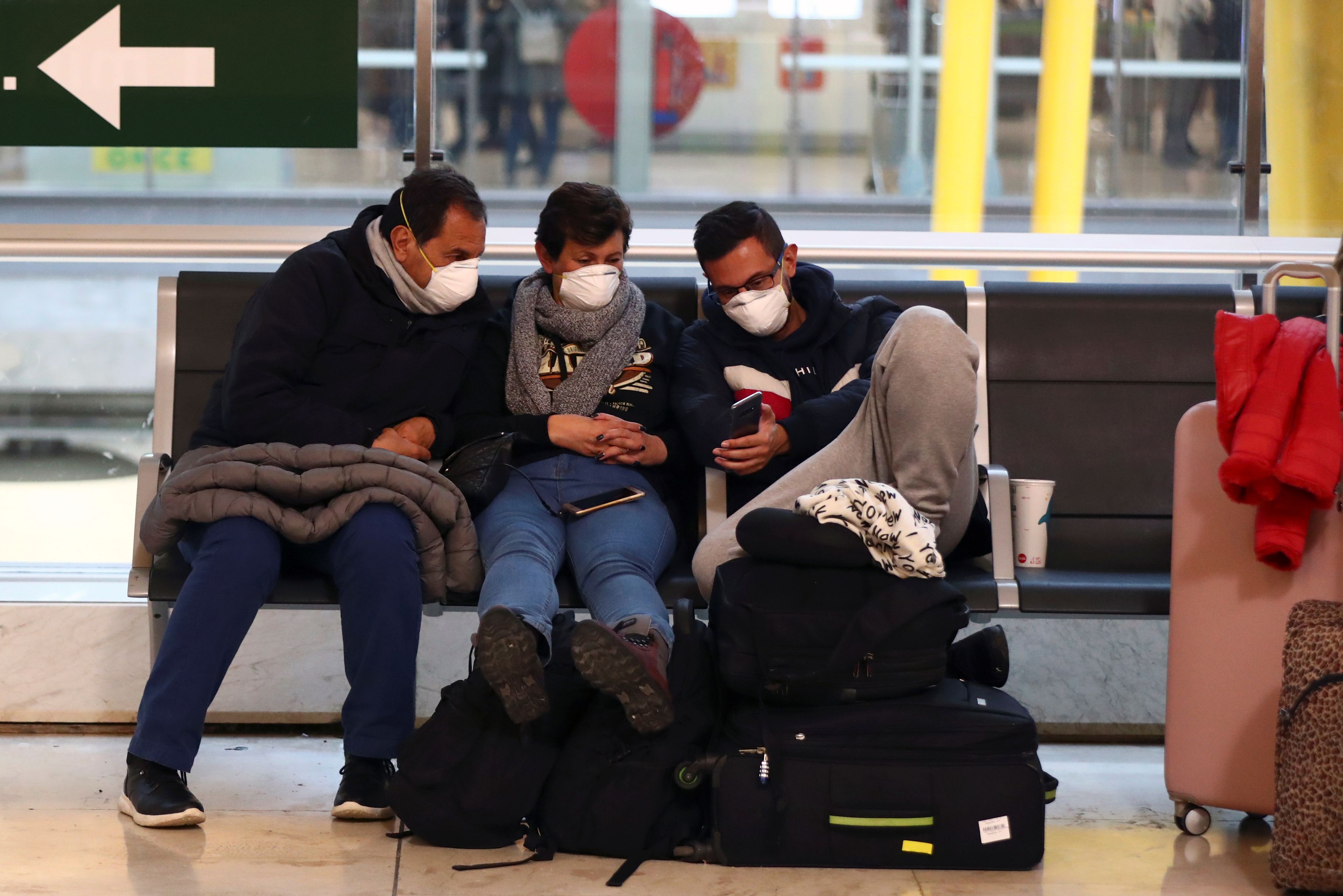 Tres hombres miran su teléfono móvil en el aeropuerto de Barajas.