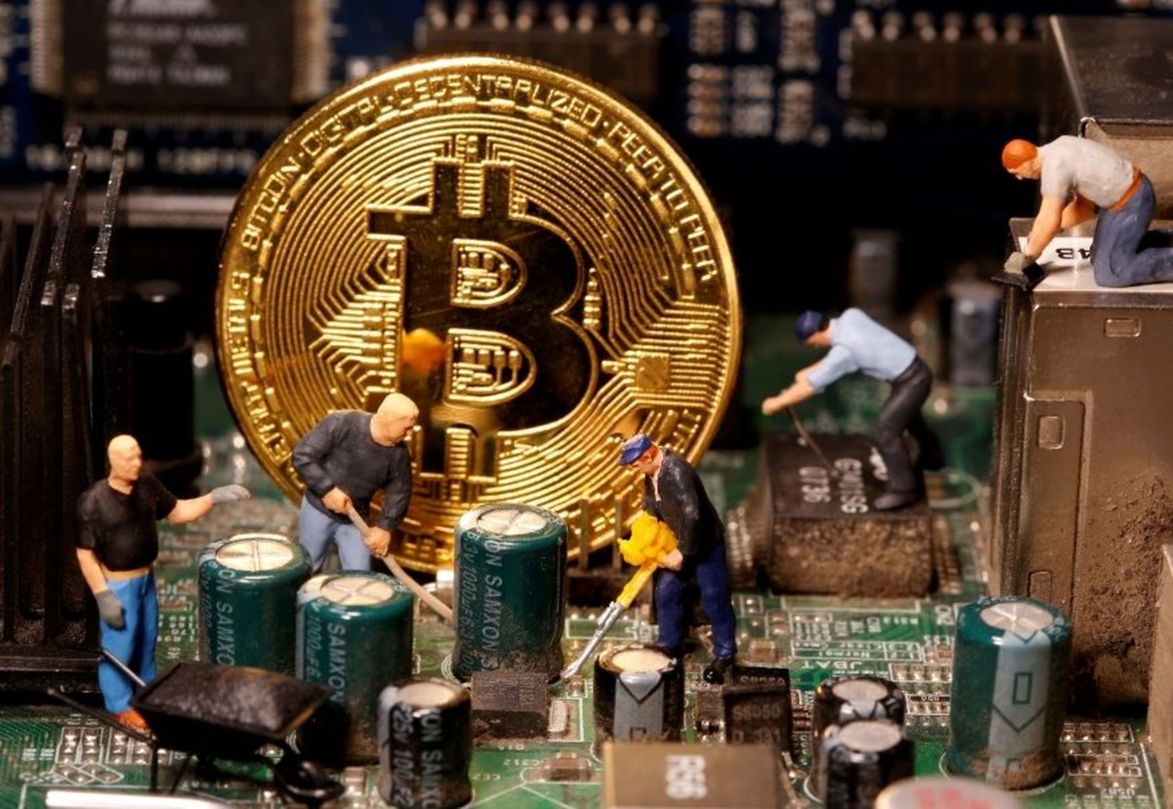 Varias figuras de trabajadores y un bitcoin en la placa base de un ordenador.