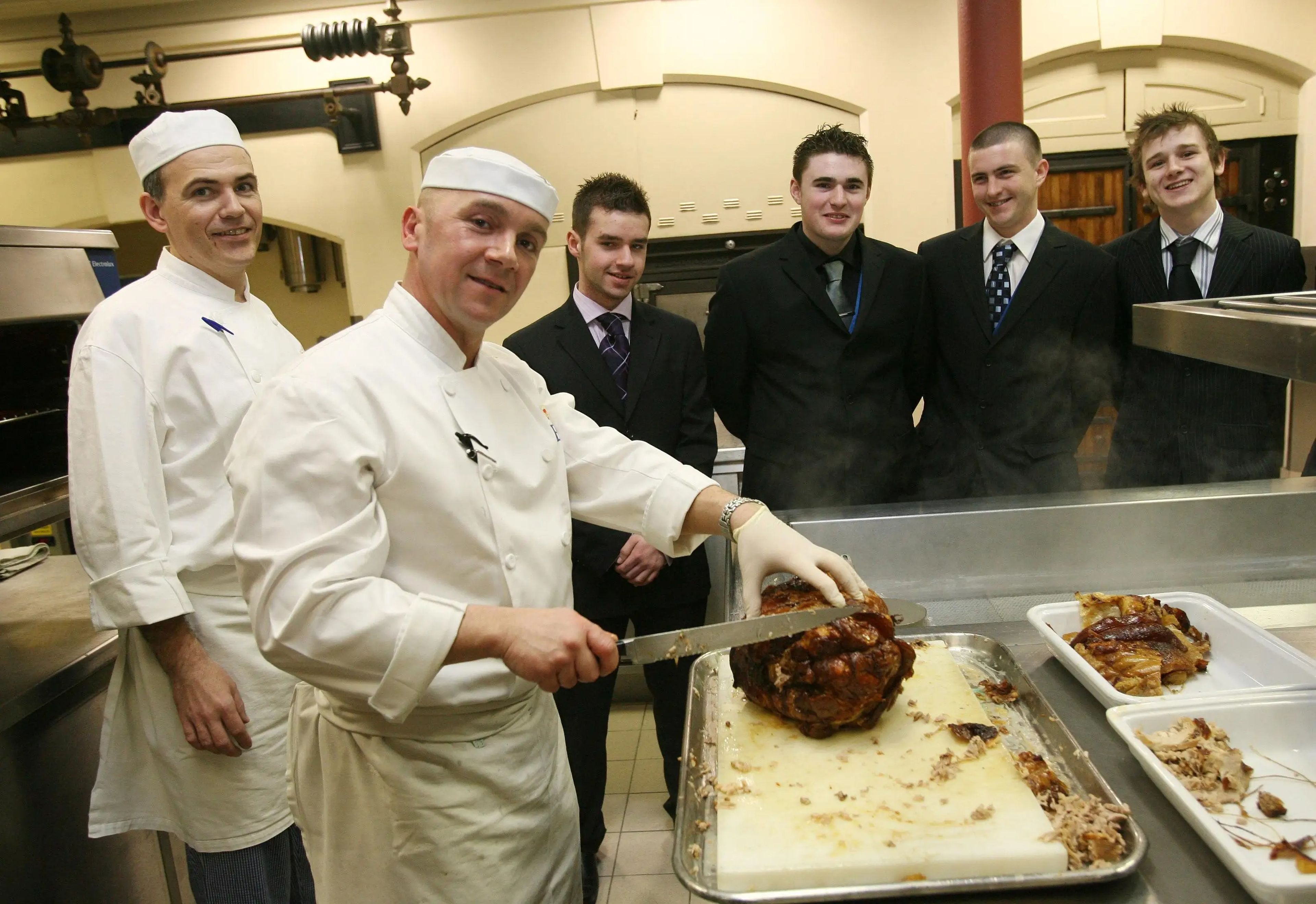 El jefe de cocina de la casa real William Barrie (segundo desde la izquierda) y el chef real Mark Flanagan (izquierda) ofrecen a los jóvenes chefs un recorrido por las cocinas del Palacio de Buckingham en 2007.