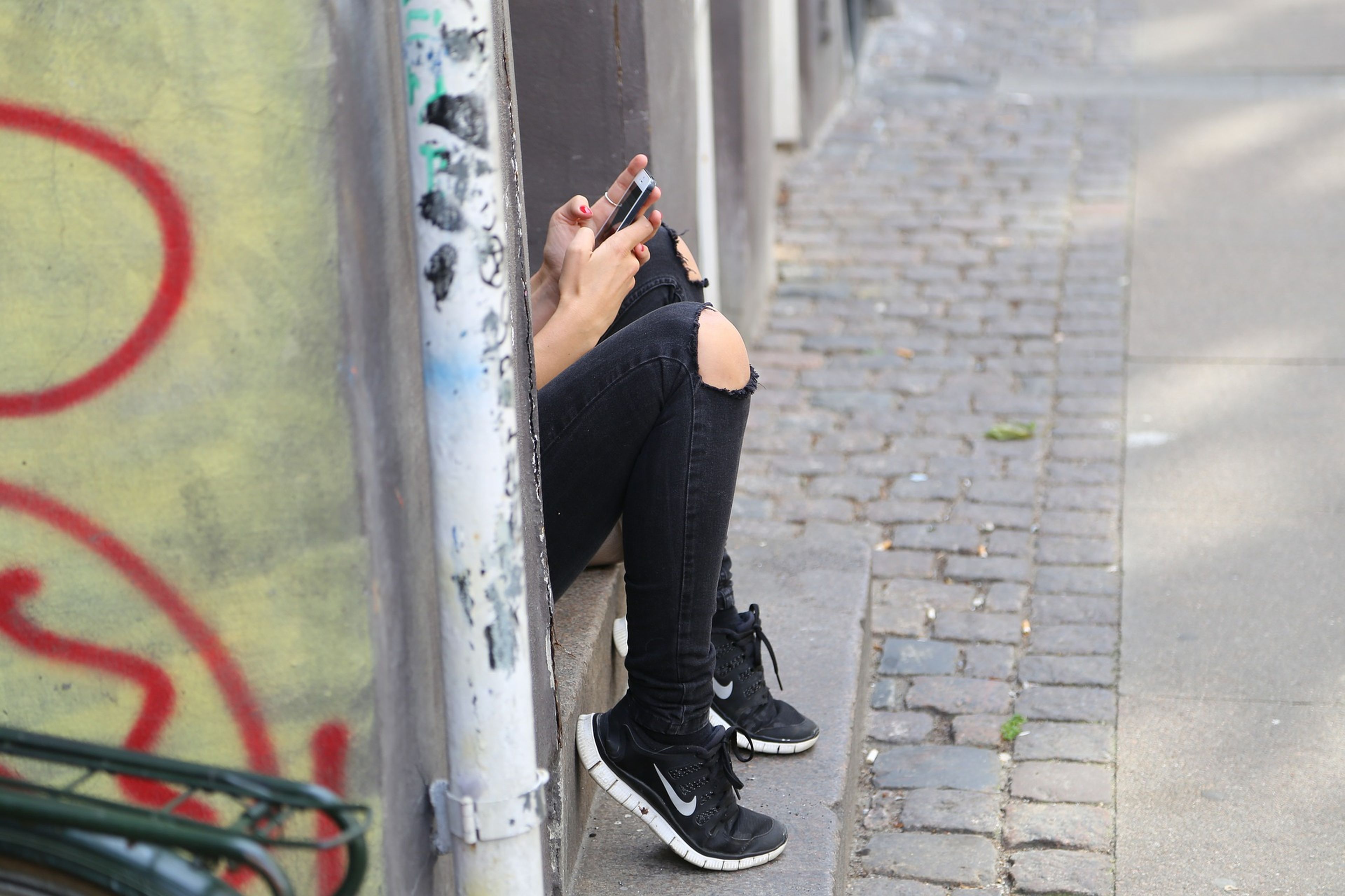 Una chica oculta tras un muro usando el móvil