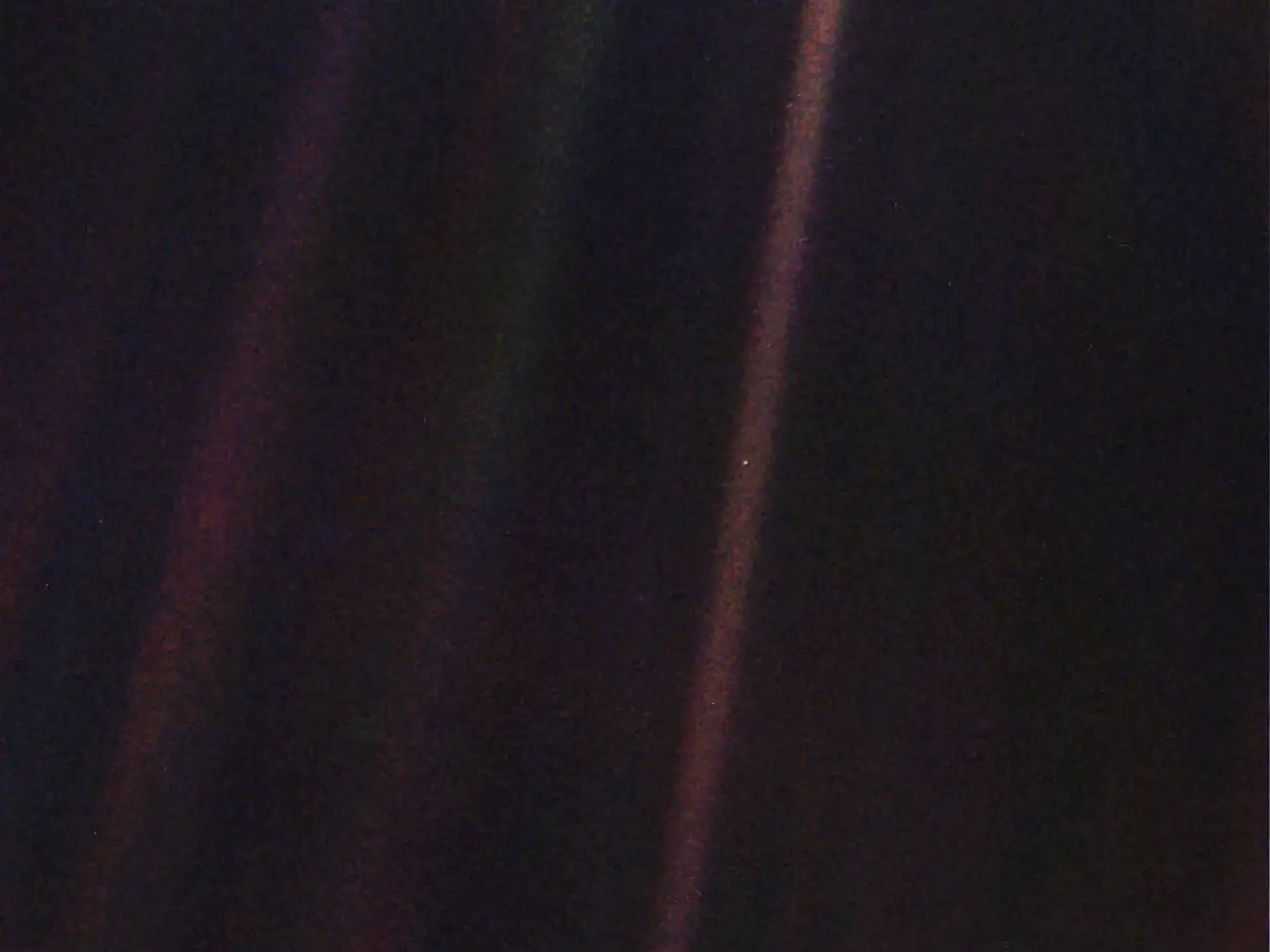 La imagen original de Pale Blue Dot, publicada el 14 de febrero de 1990. La Tierra es visible como una mancha brillante dentro del rayo de Sol justo a la derecha del centro.
