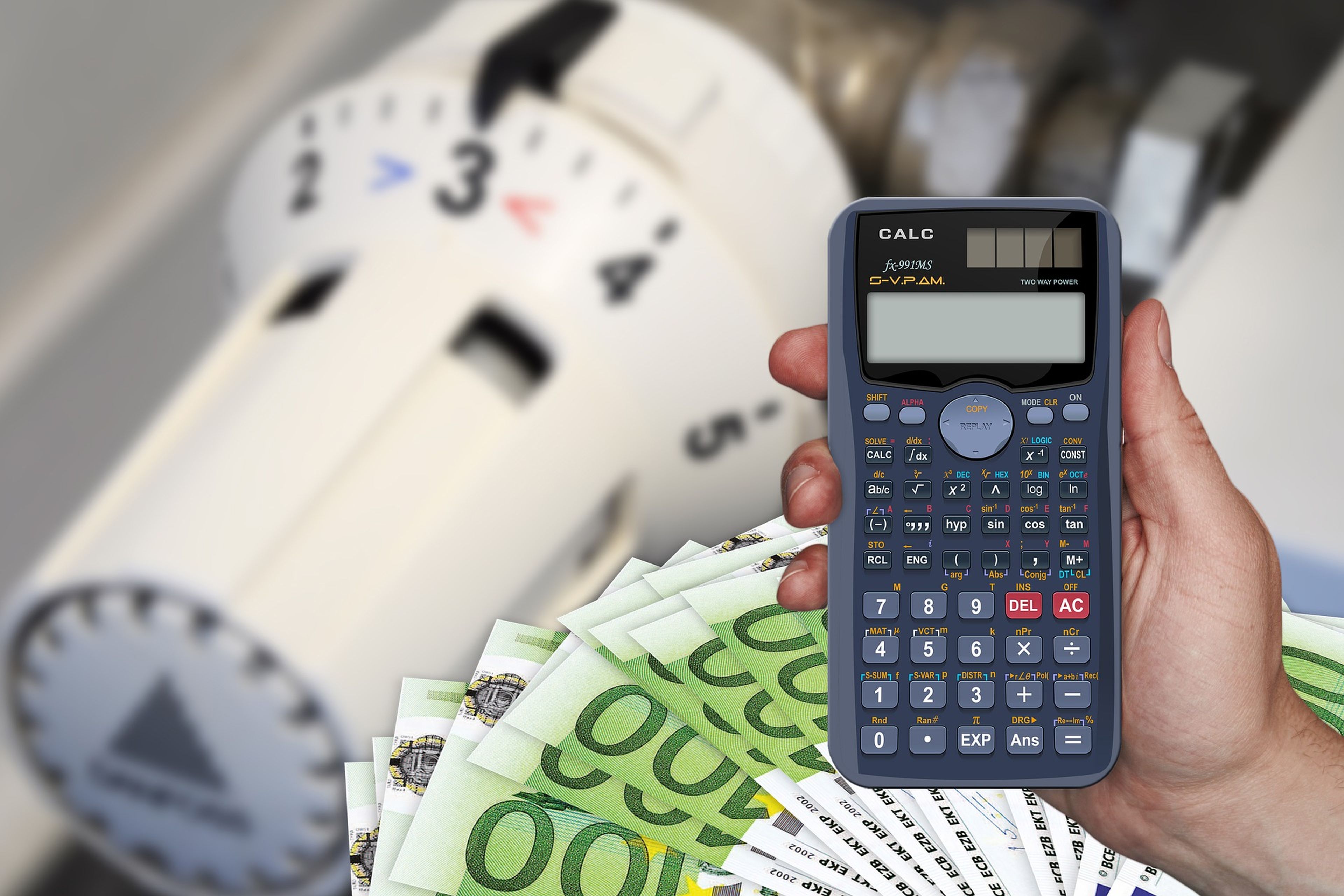 Una persona sujeta una calculadora encima de varios billetes de 100 euros y de un radiador.