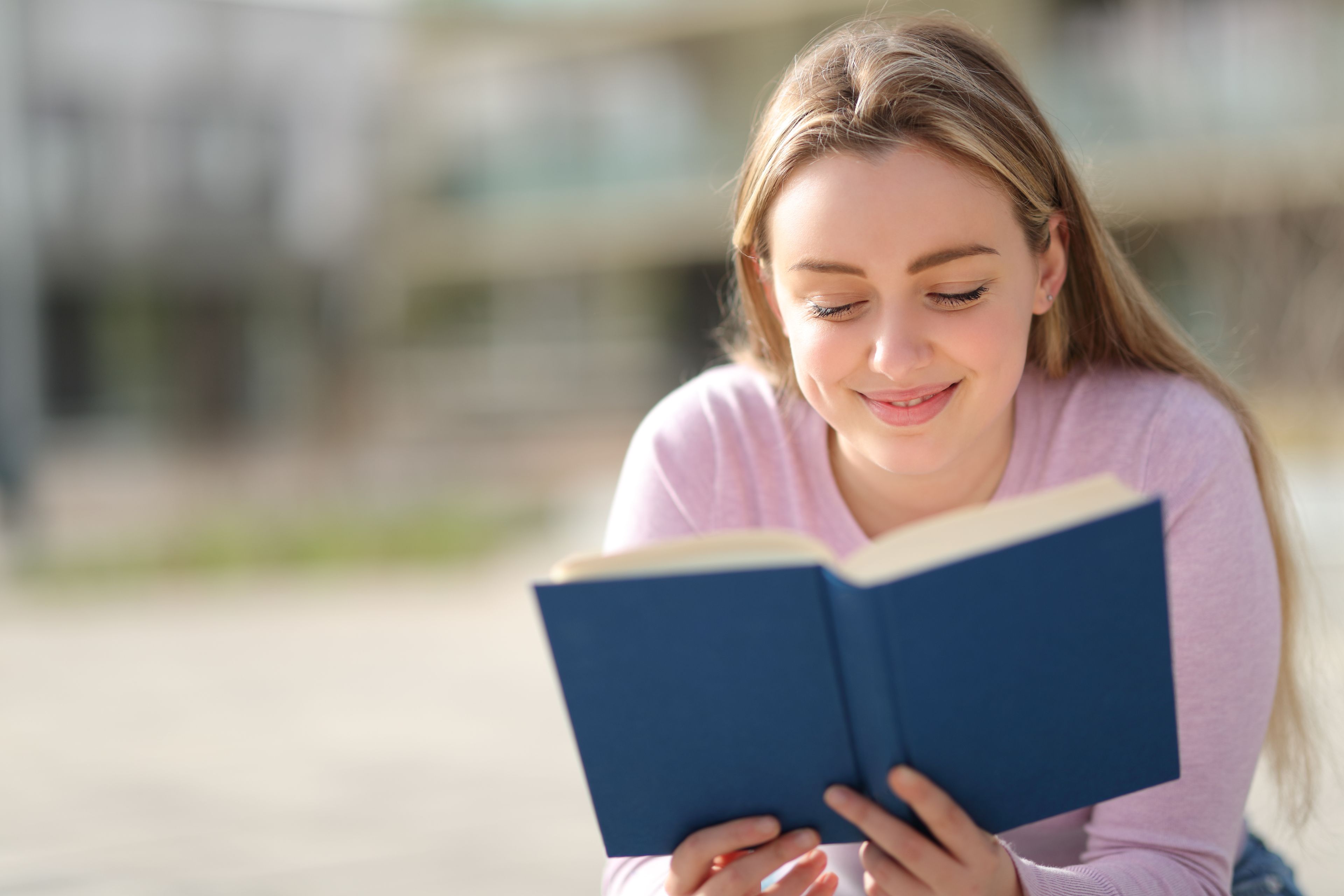 Adolescente leyendo libro de papel sentado en un parque