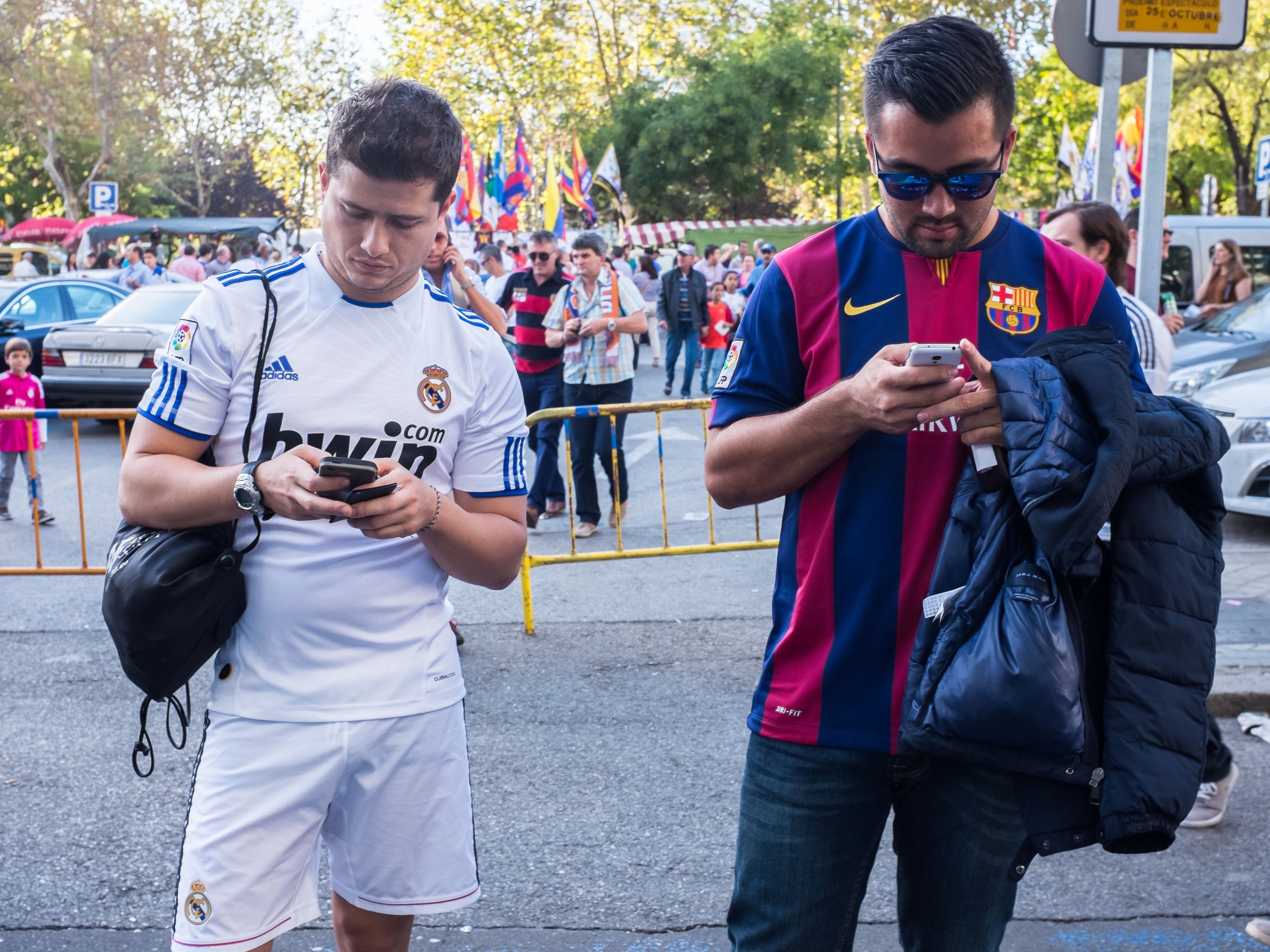Dos aficionados del Real Madrid y del Fútbol Club Barcelona miran sus smartphones.