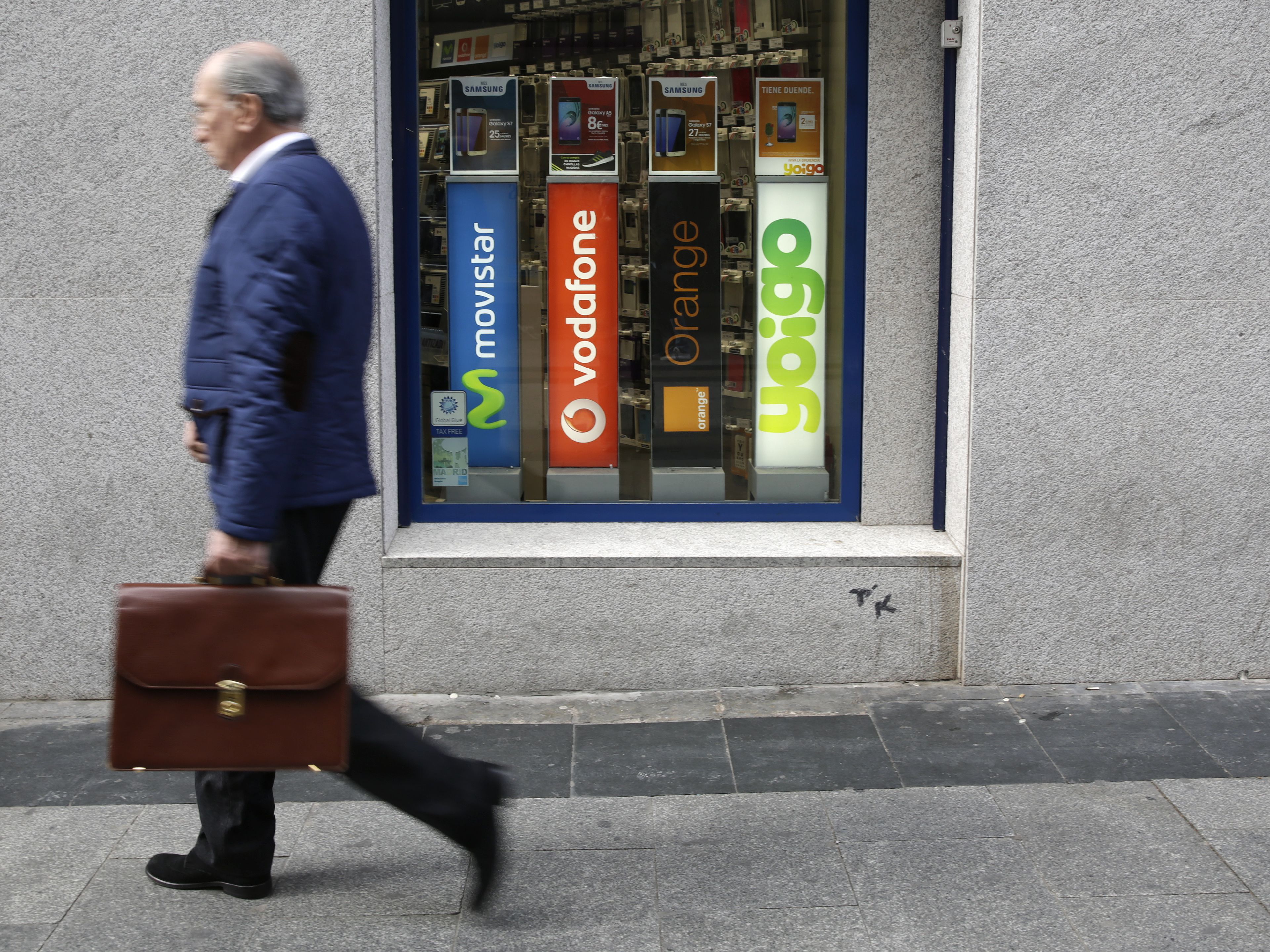 Un hombre pasea al lado de un cartel con varios logos de empresas de telecomunicaciones