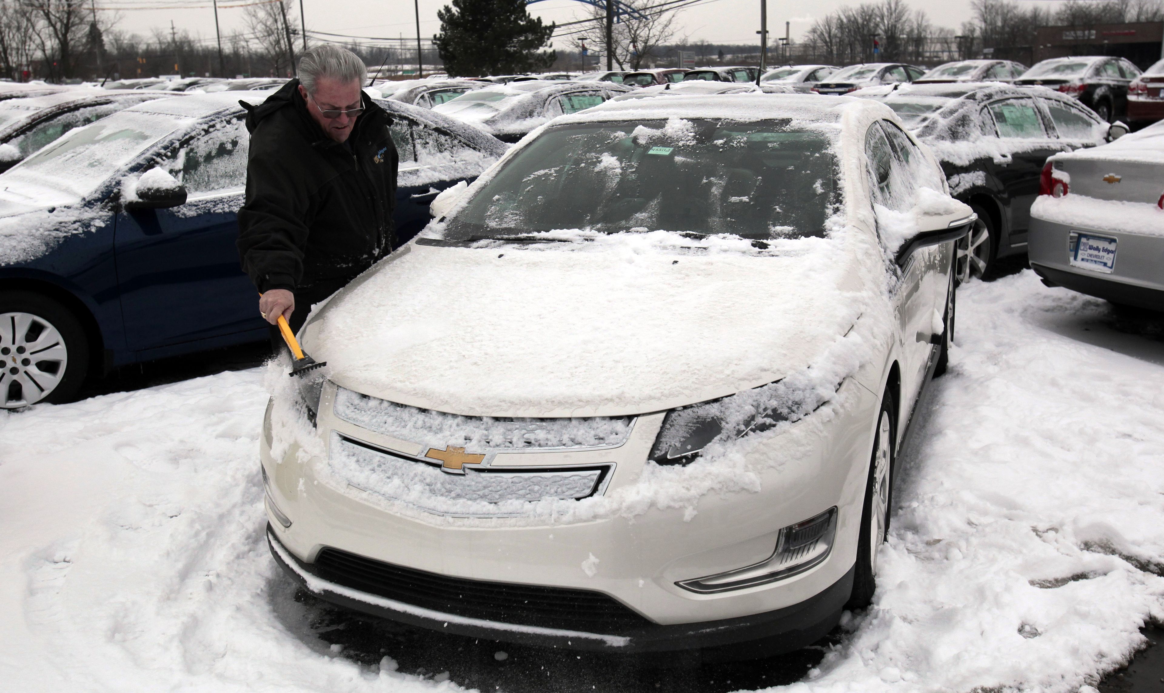 Un hombre quita la nieve de un coche eléctrico