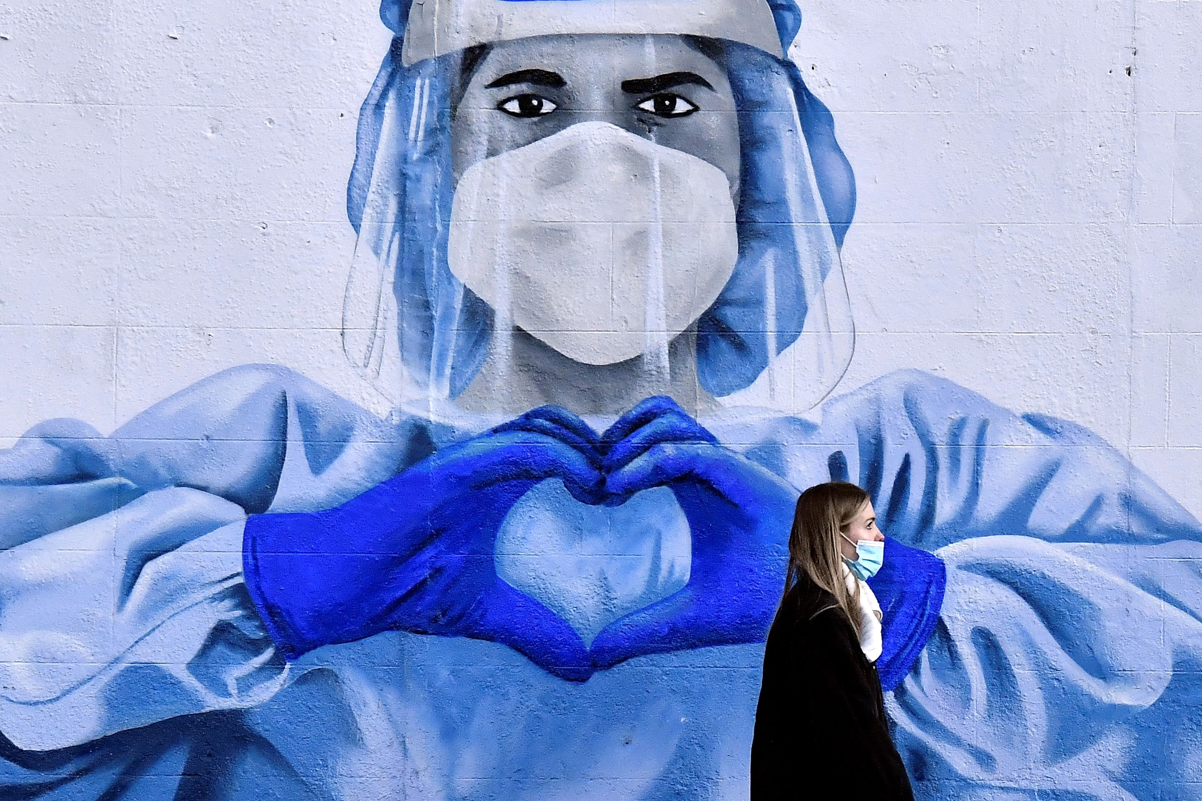 Una mujer pasa delante de un mural de apoyo a los sanitarios durante la pandemia del coronavirus