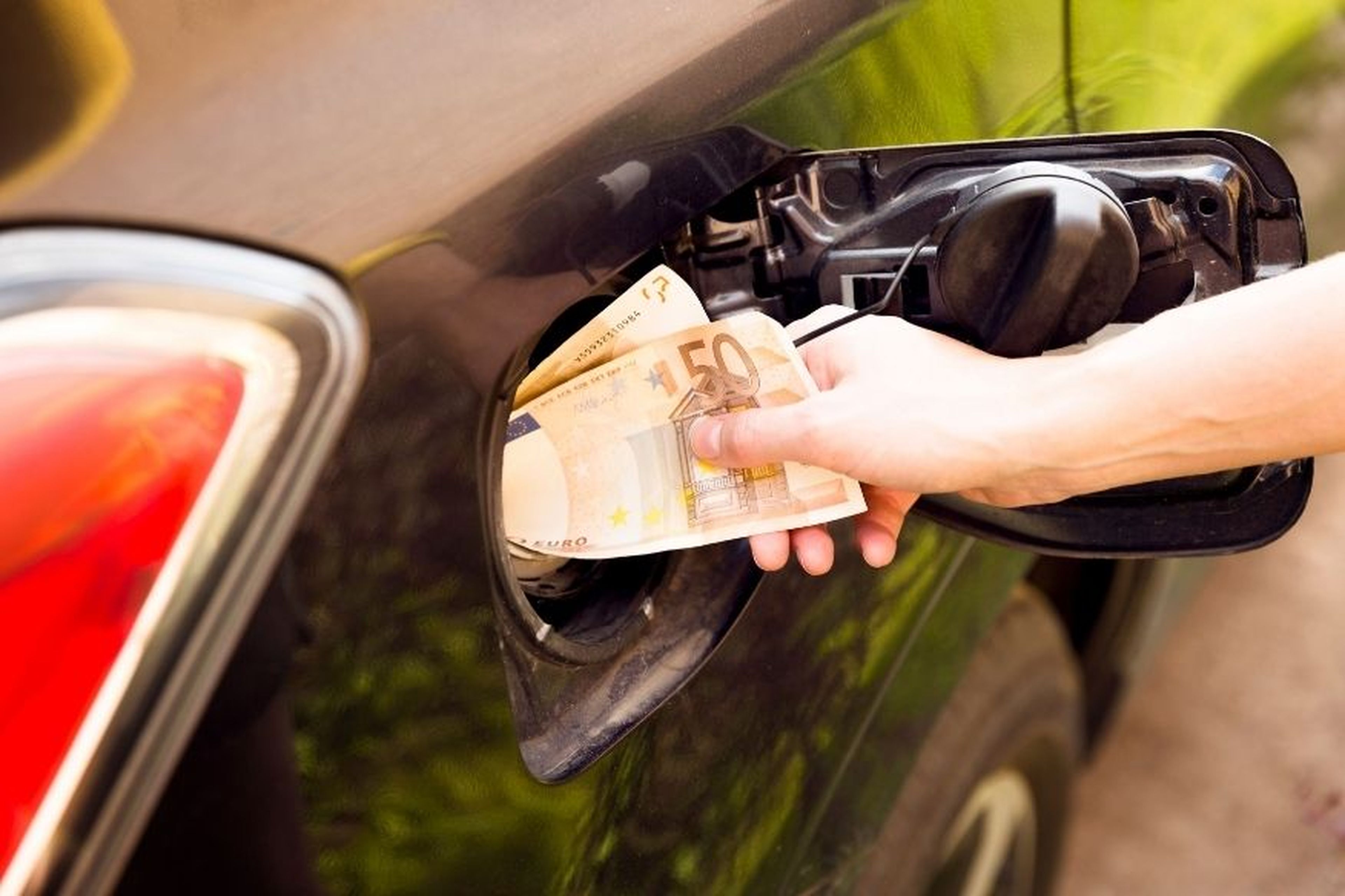 Una persona mete billetes en el depósito de gasolina.