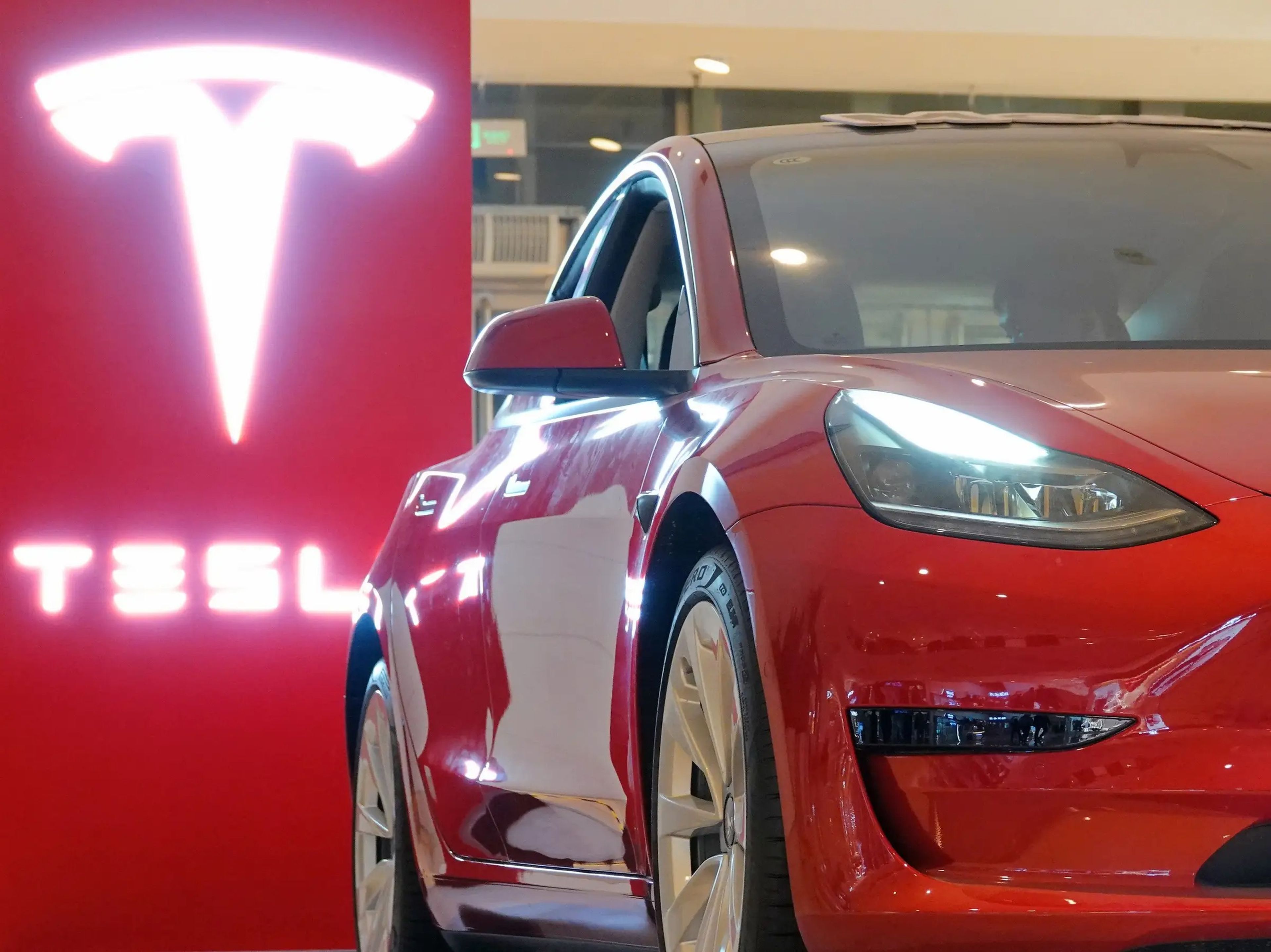 A red Tesla Model 3 in a showroom.