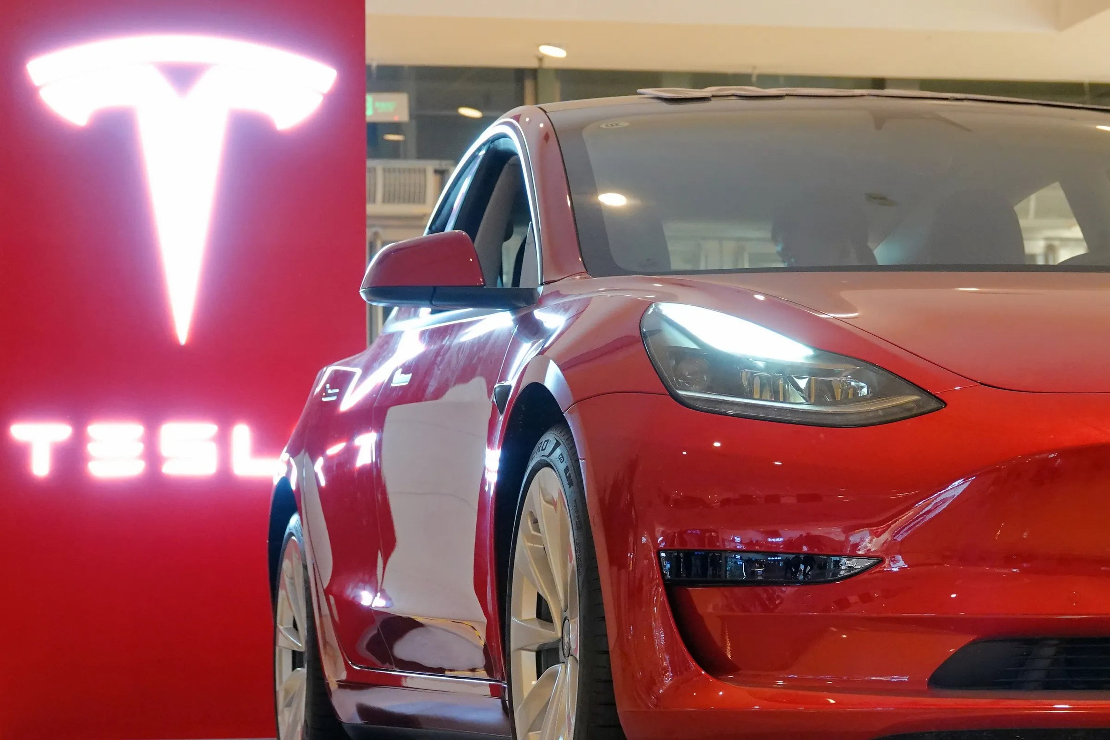A red Tesla Model 3 in a showroom.