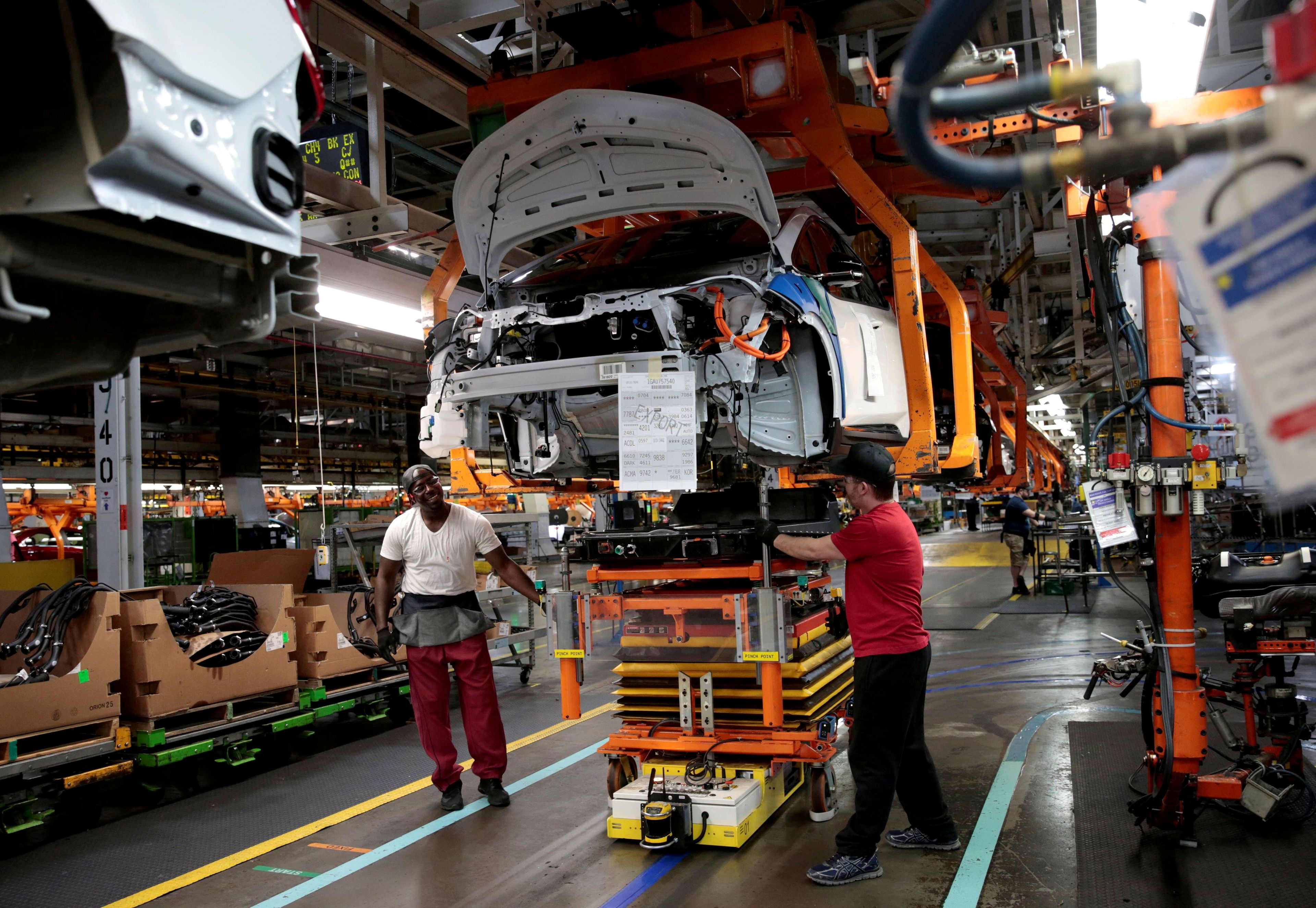 Trabajadores de la cadena de montaje de General Motors conectan un paquete de baterías debajo de un vehículo Chevrolet Bolt EV