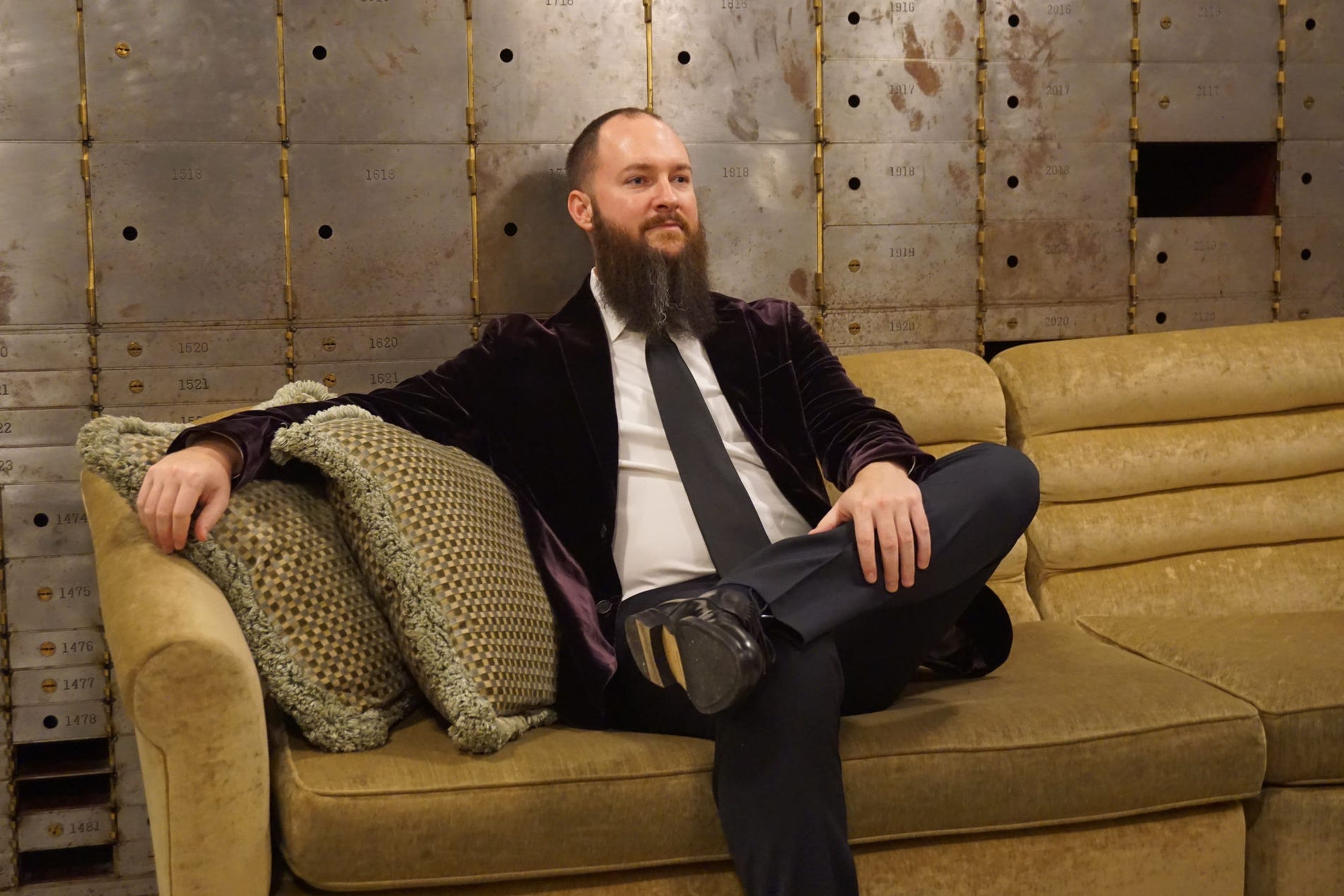 Jameson Lopp, cofundador de Casa, sentado en un sofá en una antigua cámara acorazada de un banco y vestido con un traje de etiqueta.