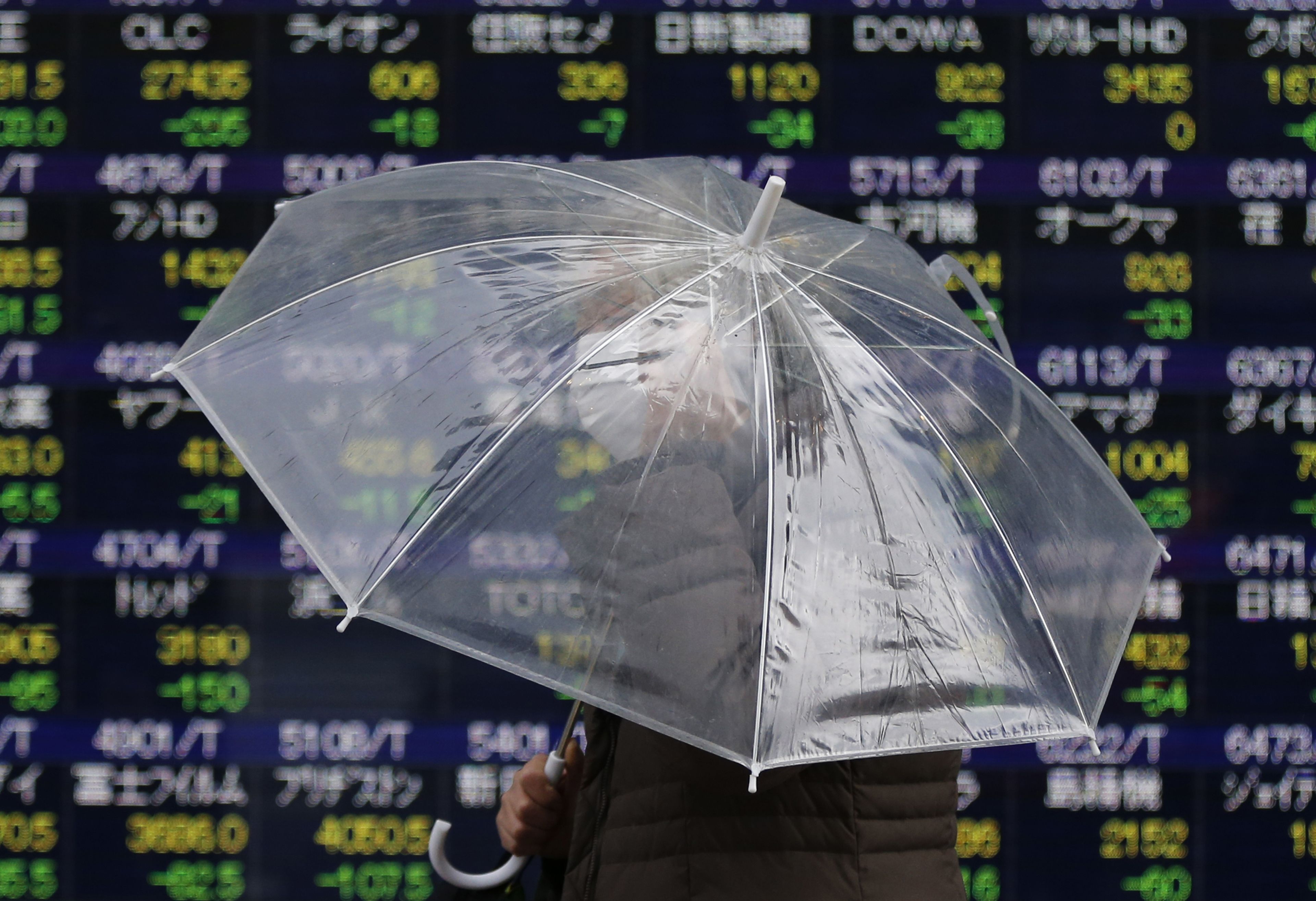 Una mujer con un paraguas frente a unos índices bursátiles