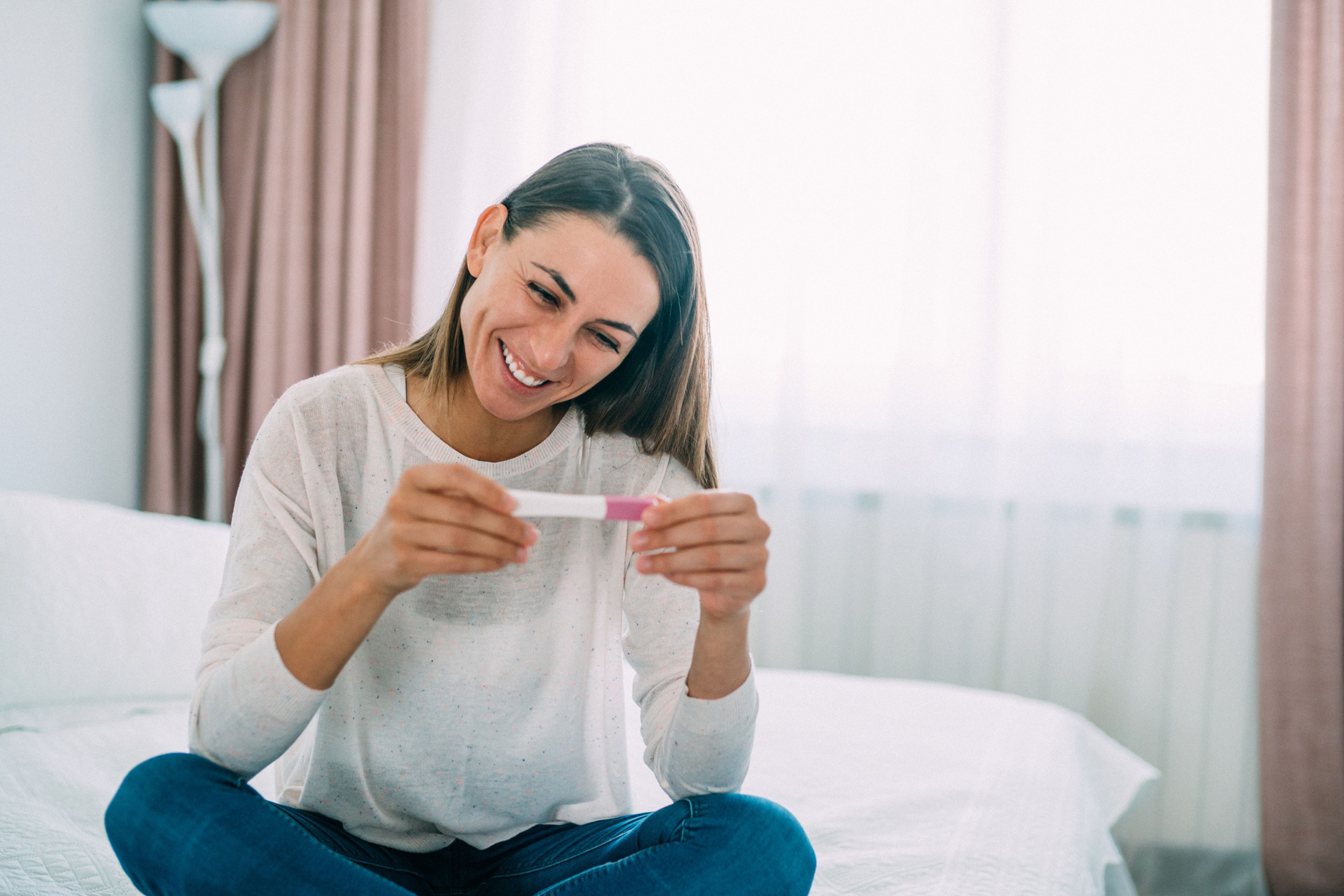 Una mujer sonriente sostiene un test de embarazo