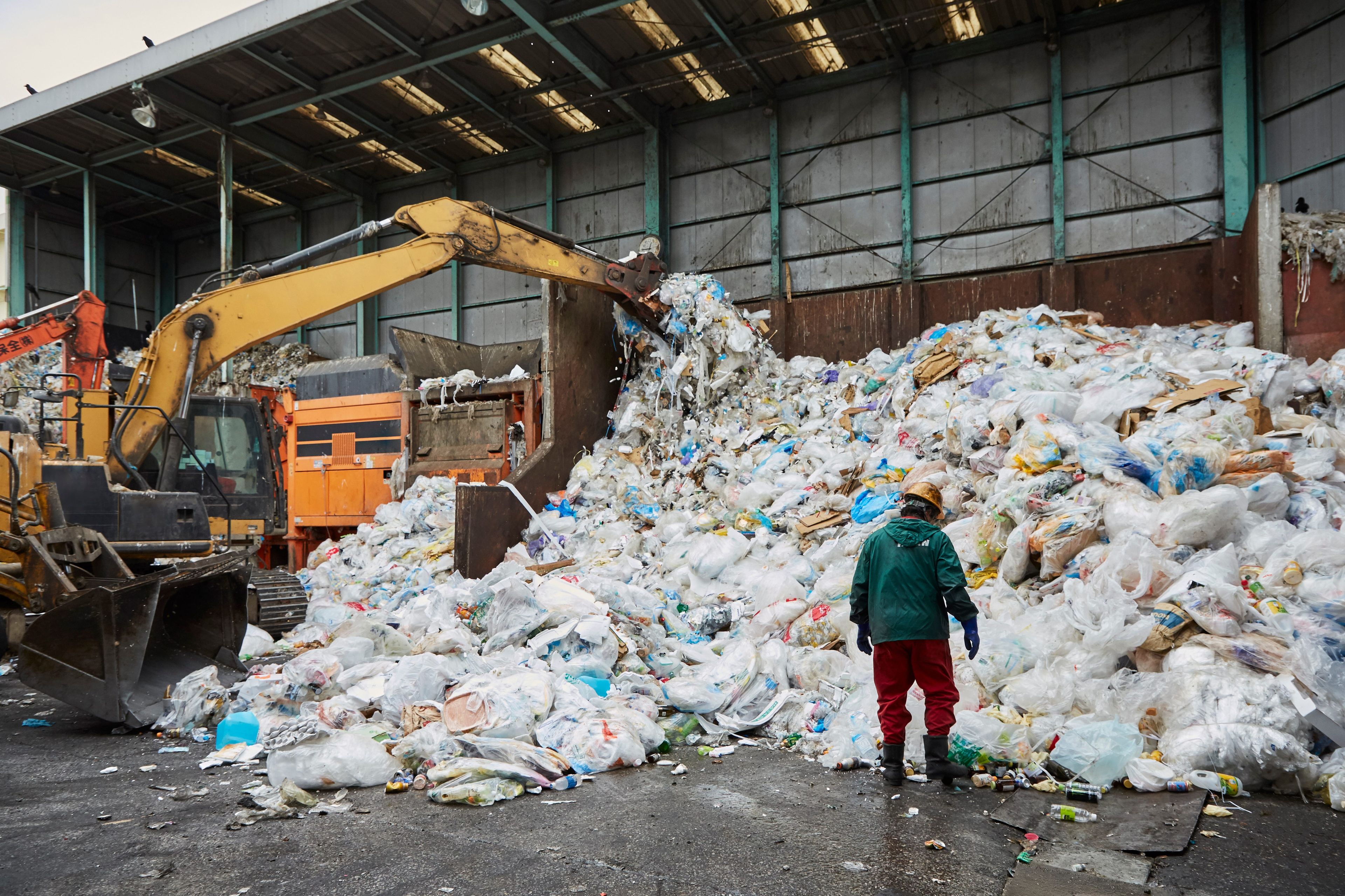 Un trabajador se para frente a una pila de desechos plásticos mientras la maquinaria los procesa en una instalación en Japón.