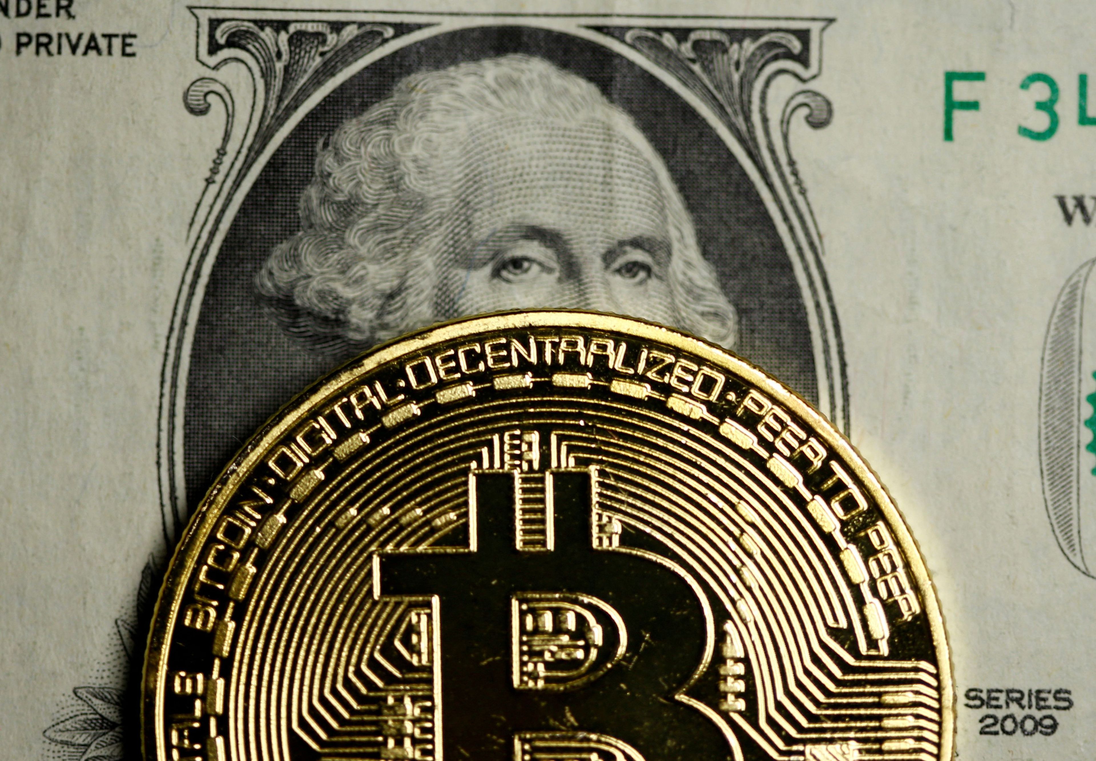 Un bitcoin delante de un billete de dólar.