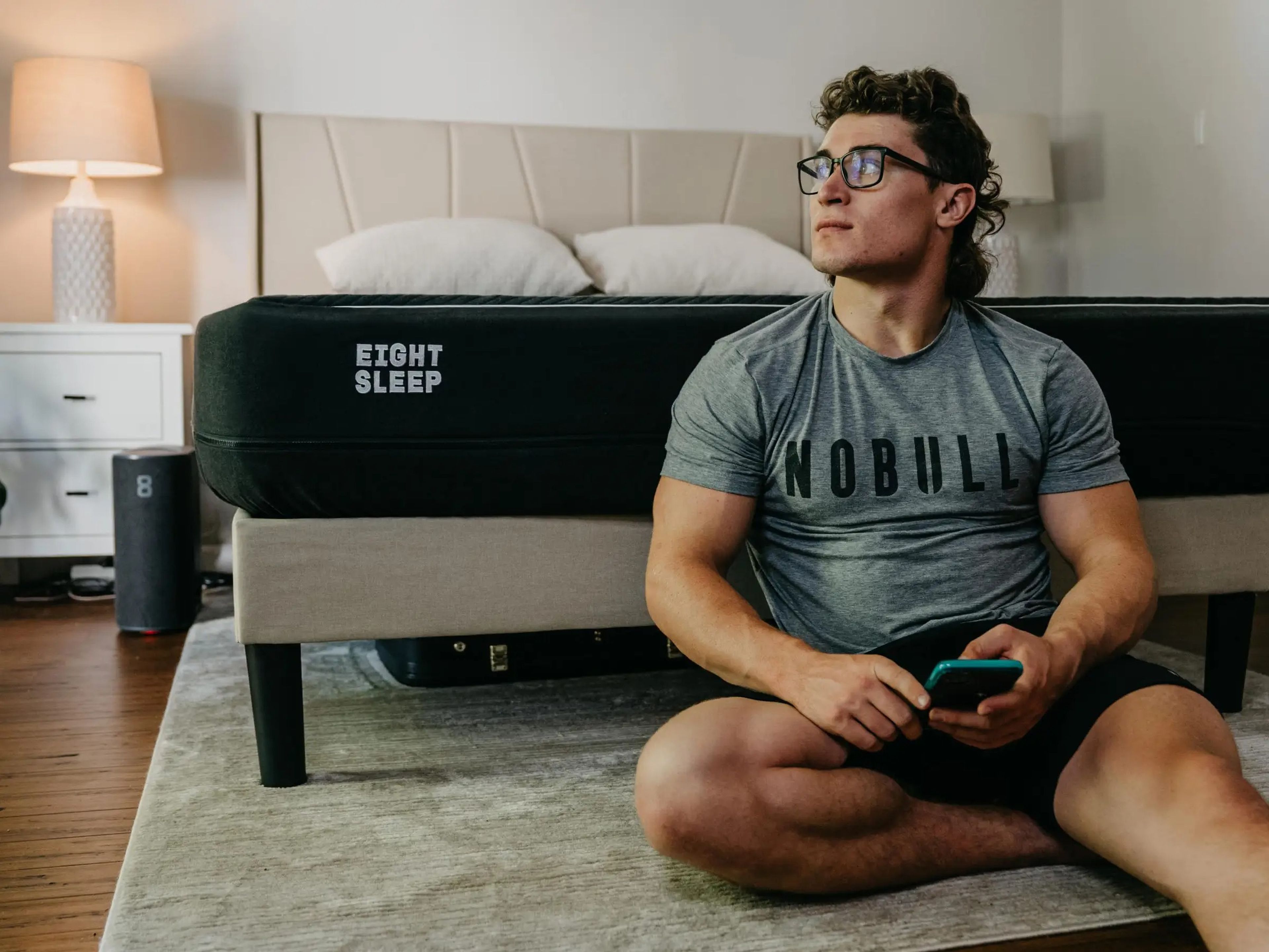 CrossFit Games athlete Justin Medeiros sitting on the floor with his back to an EightSleep brand mattress on a comfy bed