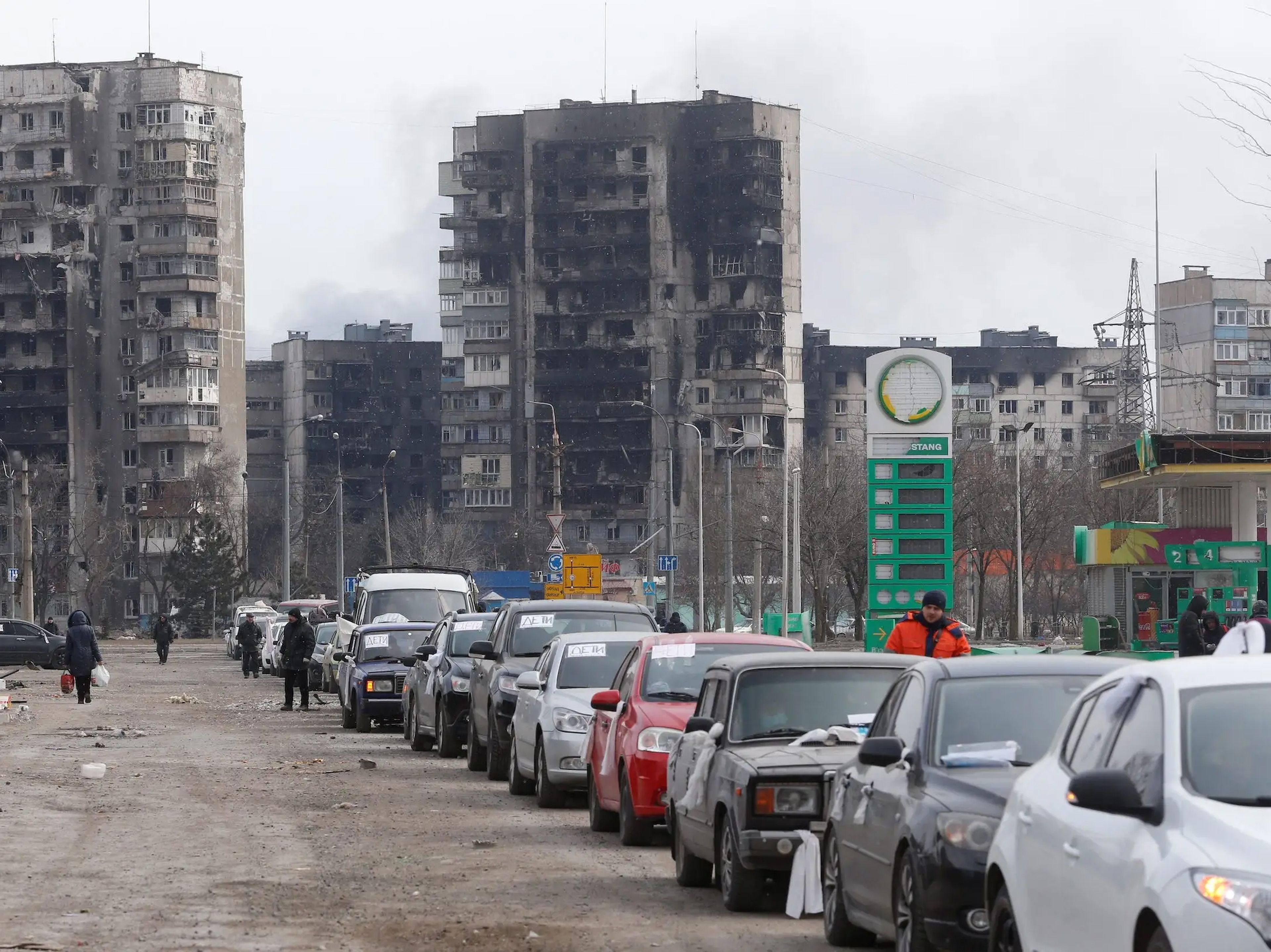 Una fila de coches deja atrás los edificios de apartamentos destruidos durante el conflicto entre Ucrania y Rusia, mientras los evacuados abandonan la ciudad portuaria asediada de Mariúpol.