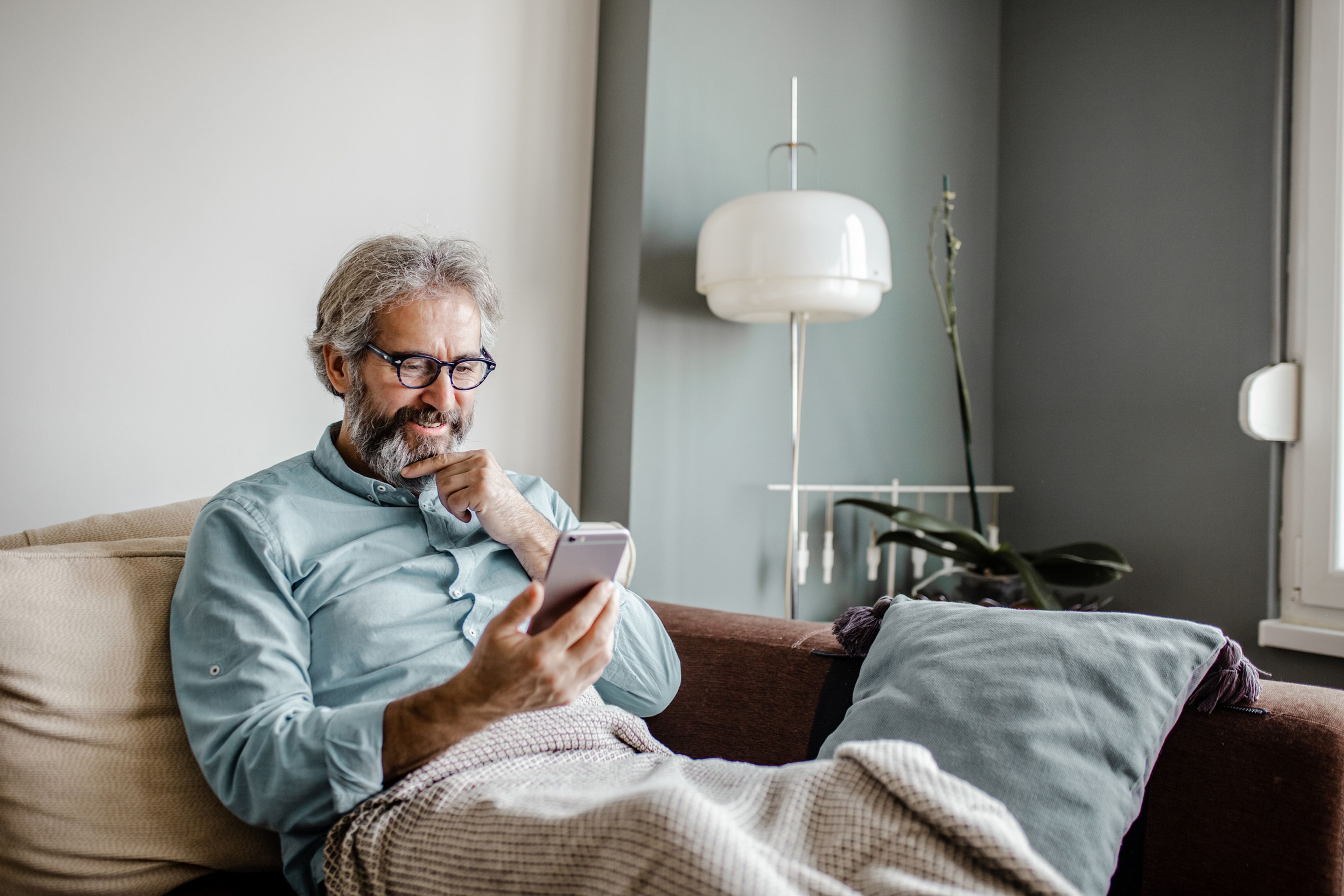 Hombre adulto mayor usa un teléfono móvil en casa, pensativo