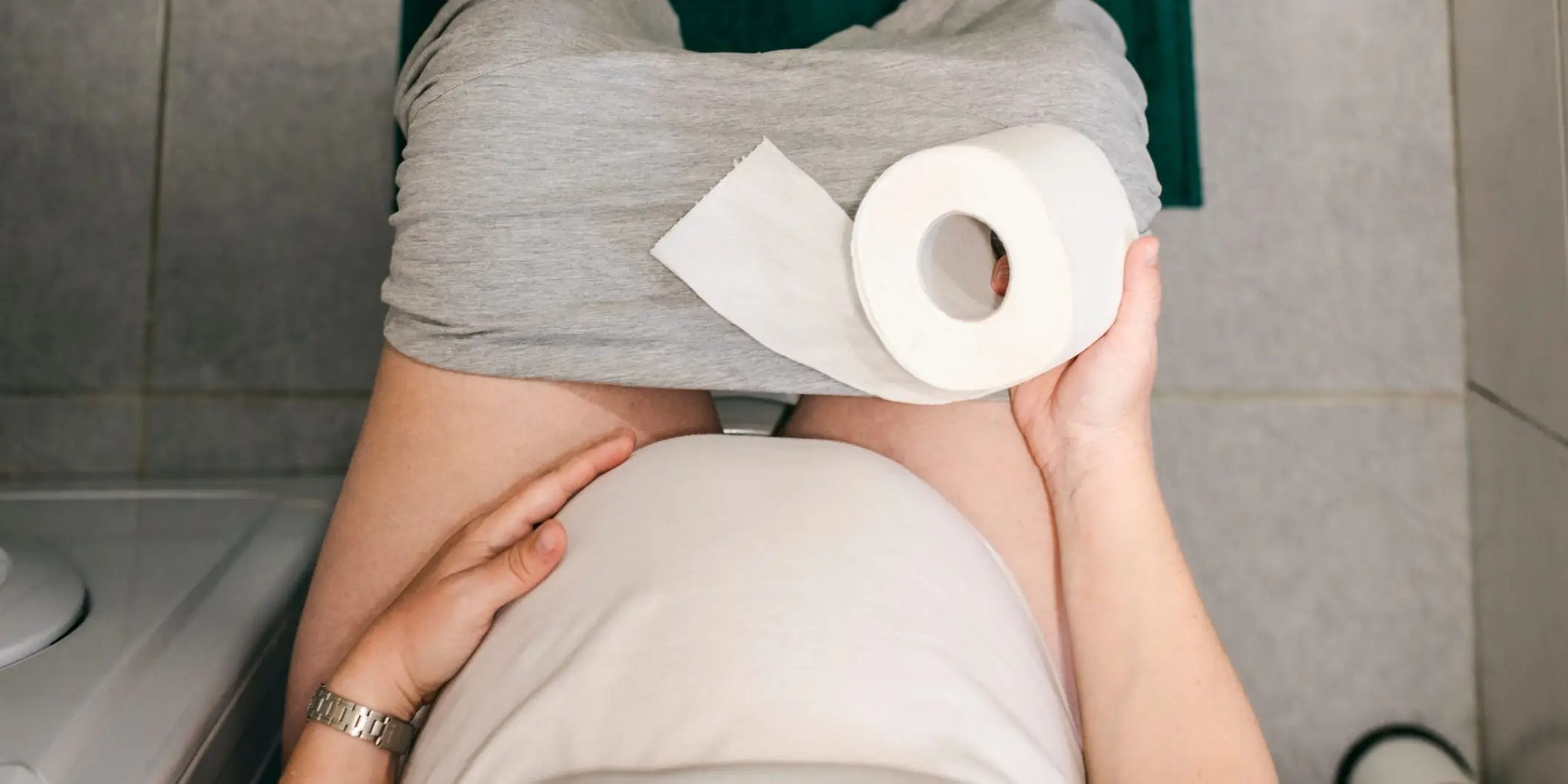 A pregnant woman sits on the toilet, constipated.