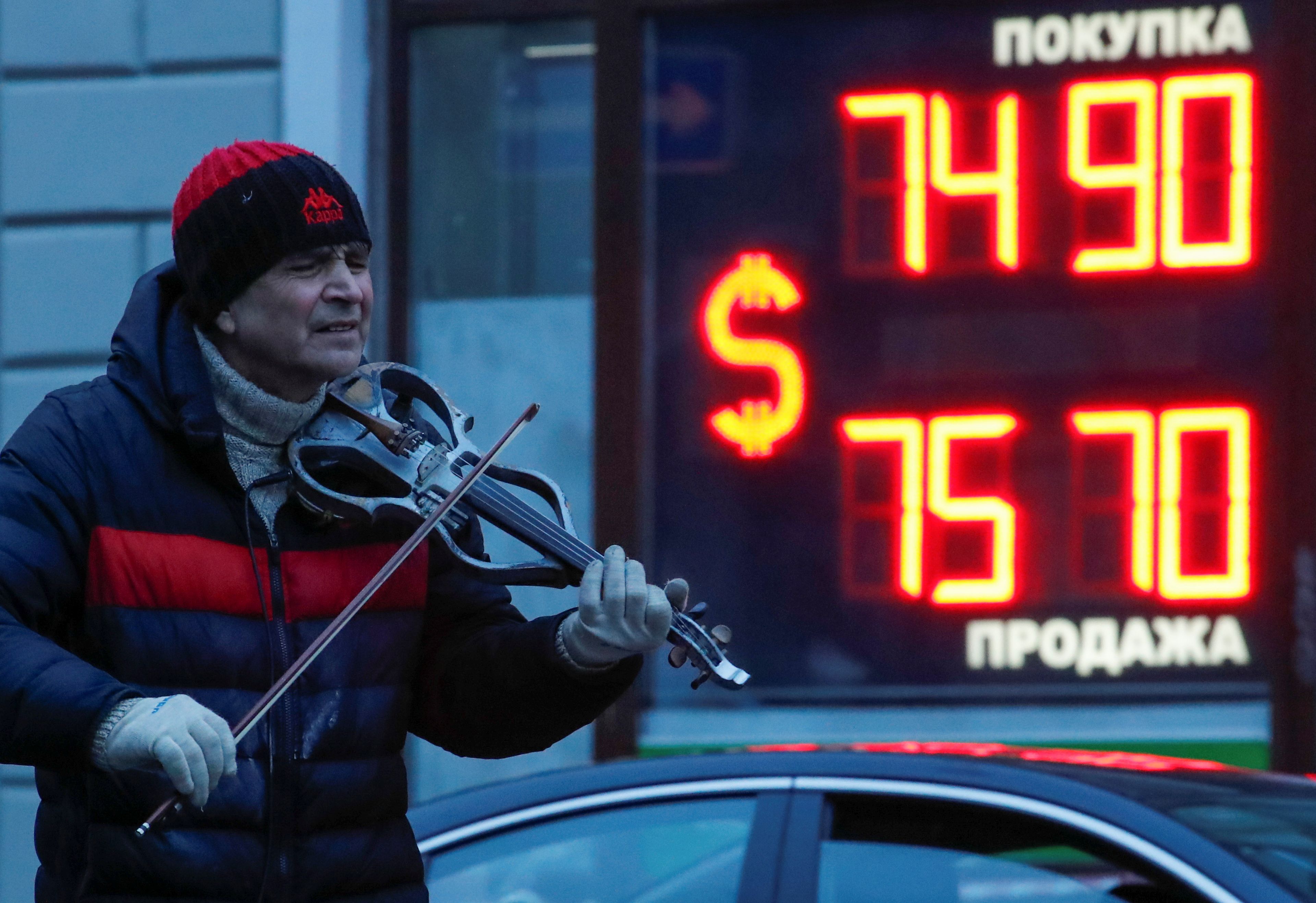 Un artista callejero toca el violín cerca de un panel que muestra los tipos de cambio en San Petersburgo.
