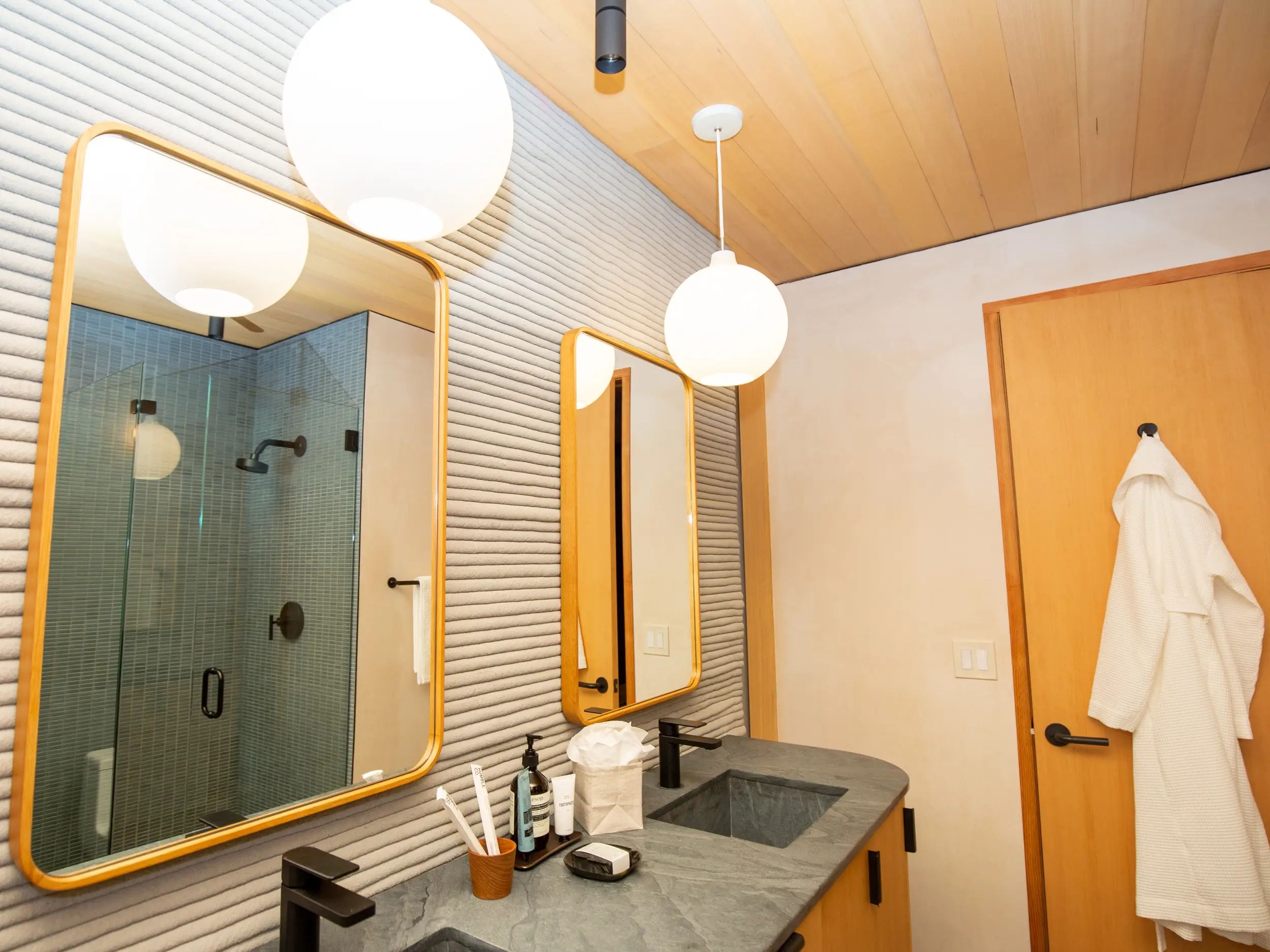 A bathroom with dual sinks, mirrors, and lights. There's a robe hanging on the wall.