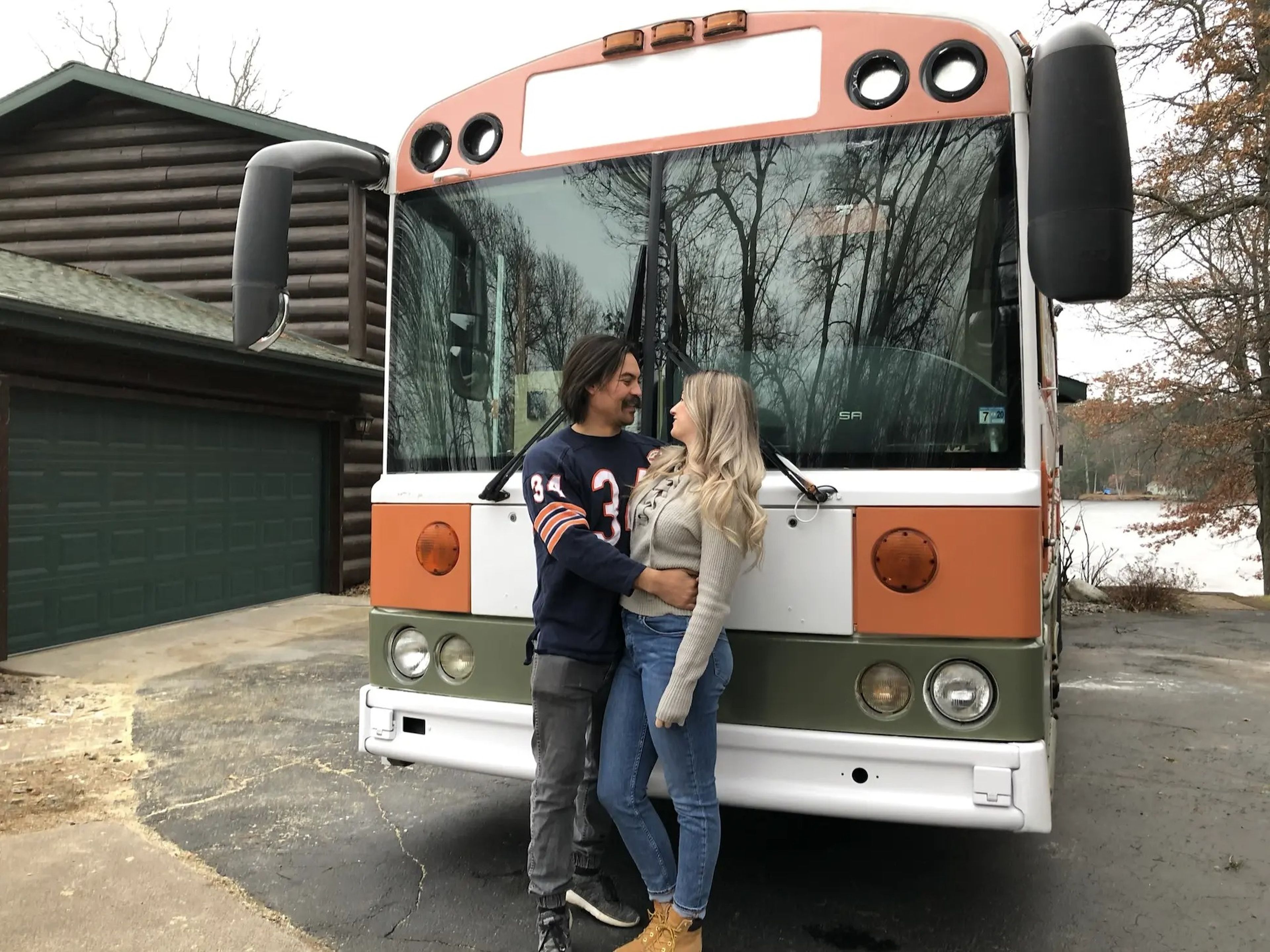 The couple posing outside of the painted orange-and-white school bus