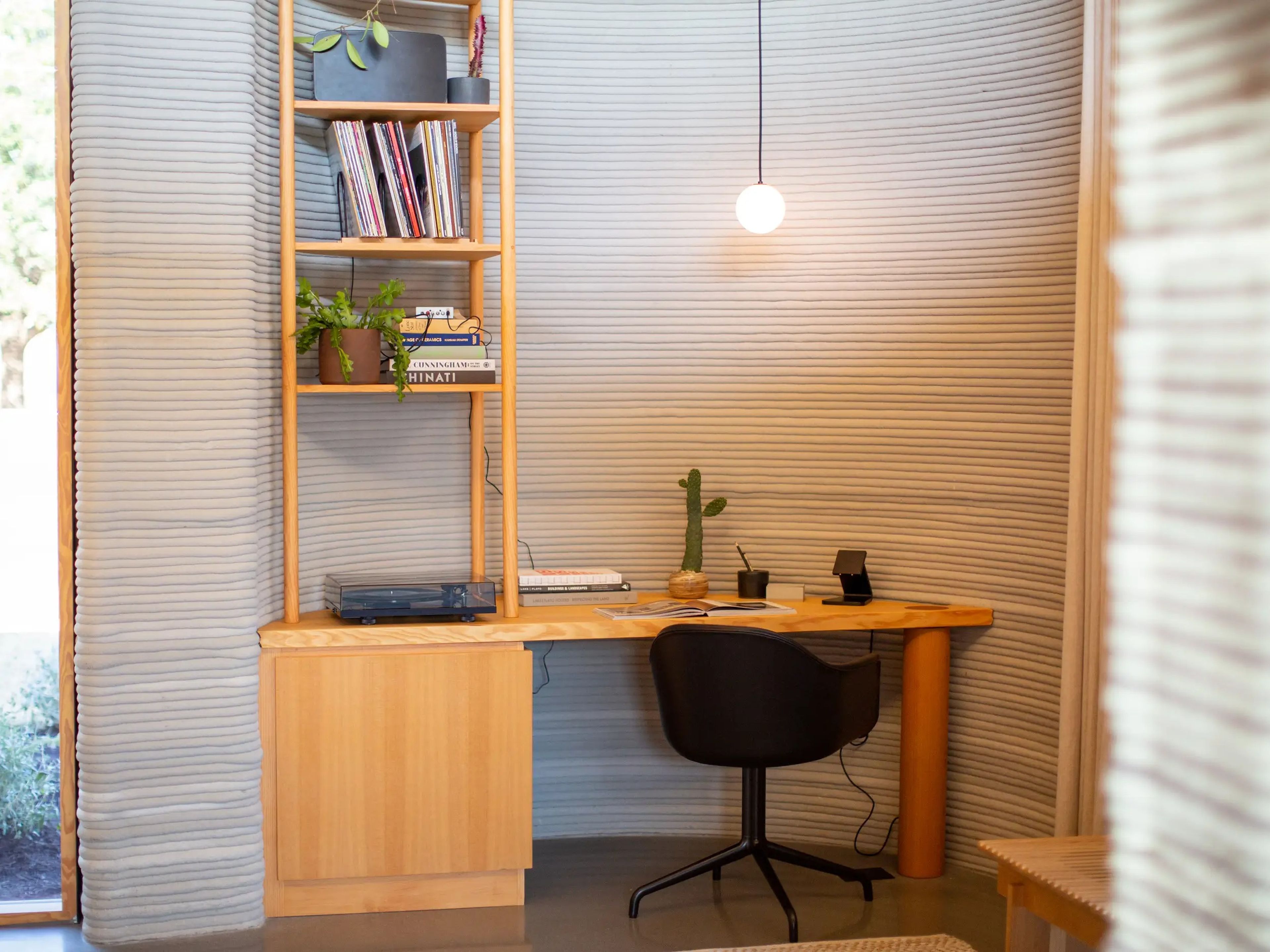 A desk in front of a 3D printed wall surrounded by windows.