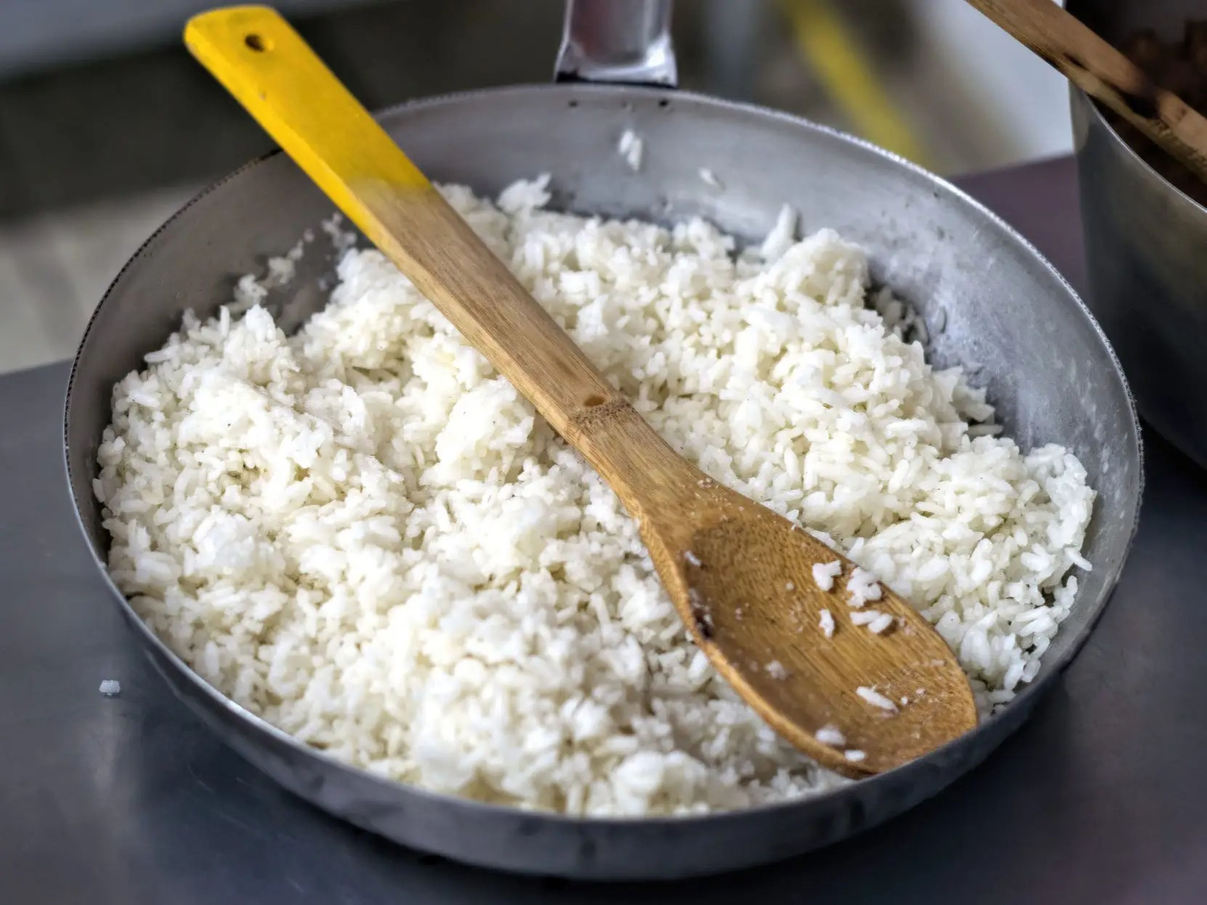 a frying pan full of cooked white rice resting on a countertop with a wooden spoon in the middle of the pan