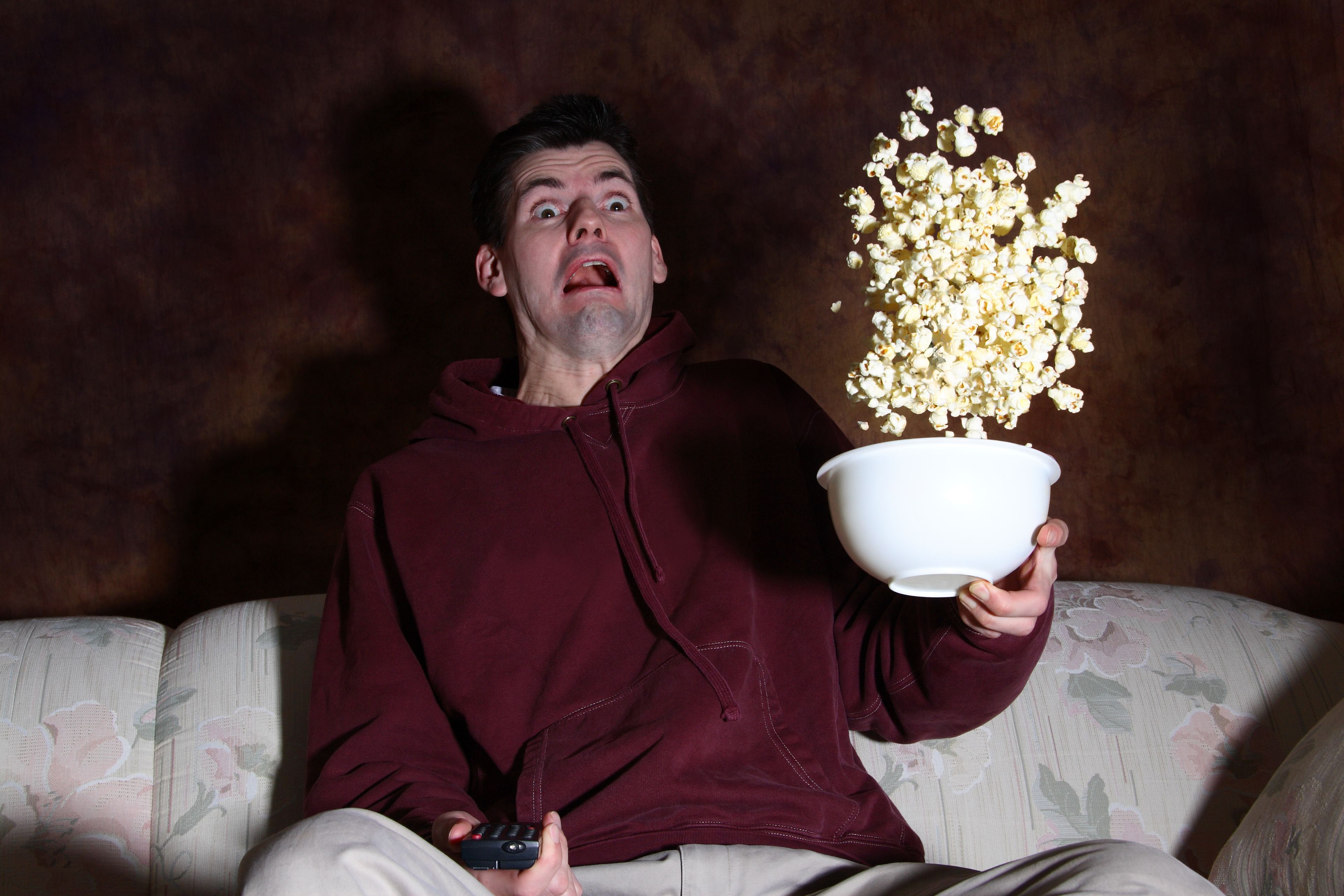 Un hombre se asusta mientras ve la televisión y come palomitas