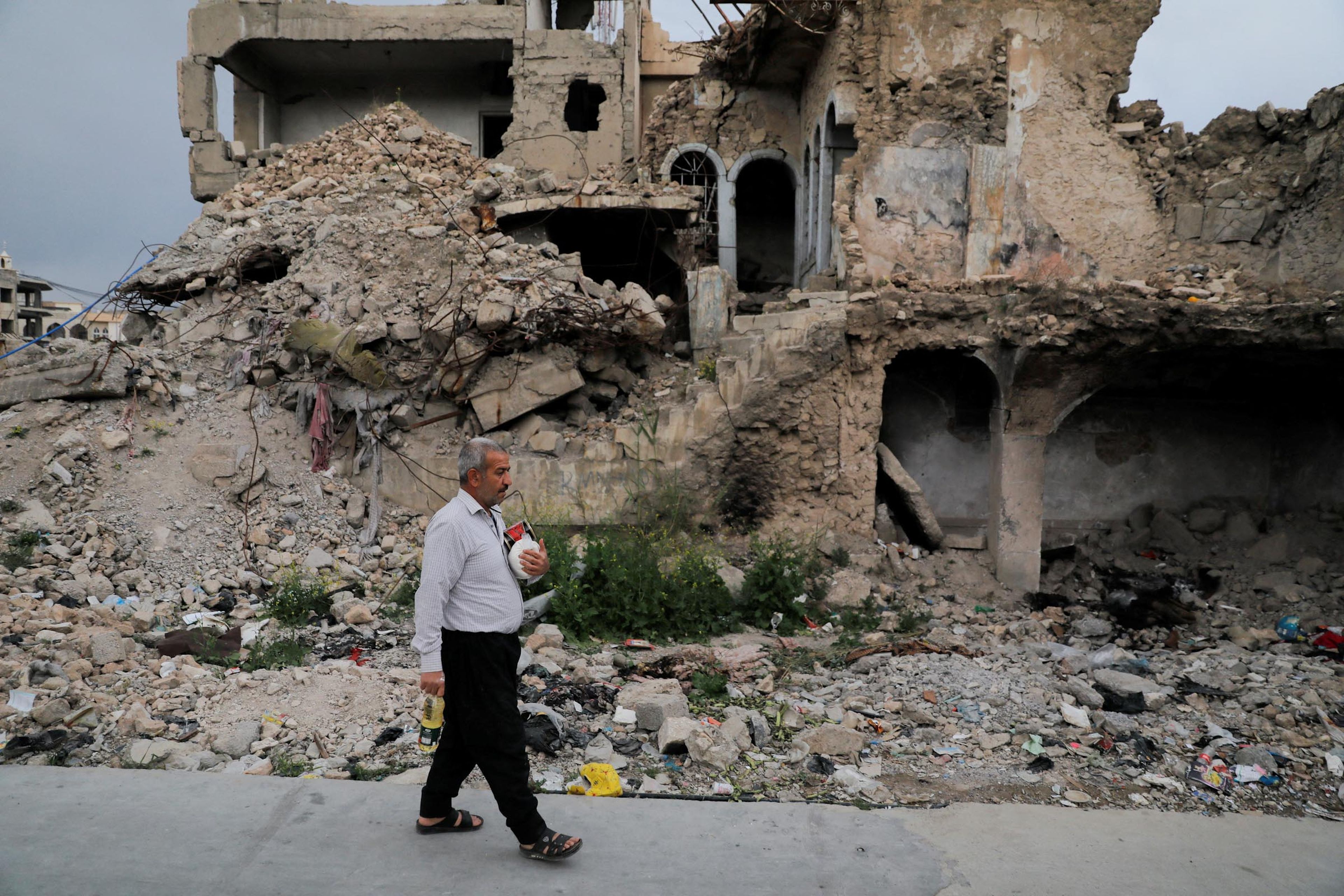 Un hombre camina entre ruinas tras comprar en el mercado, en Irak