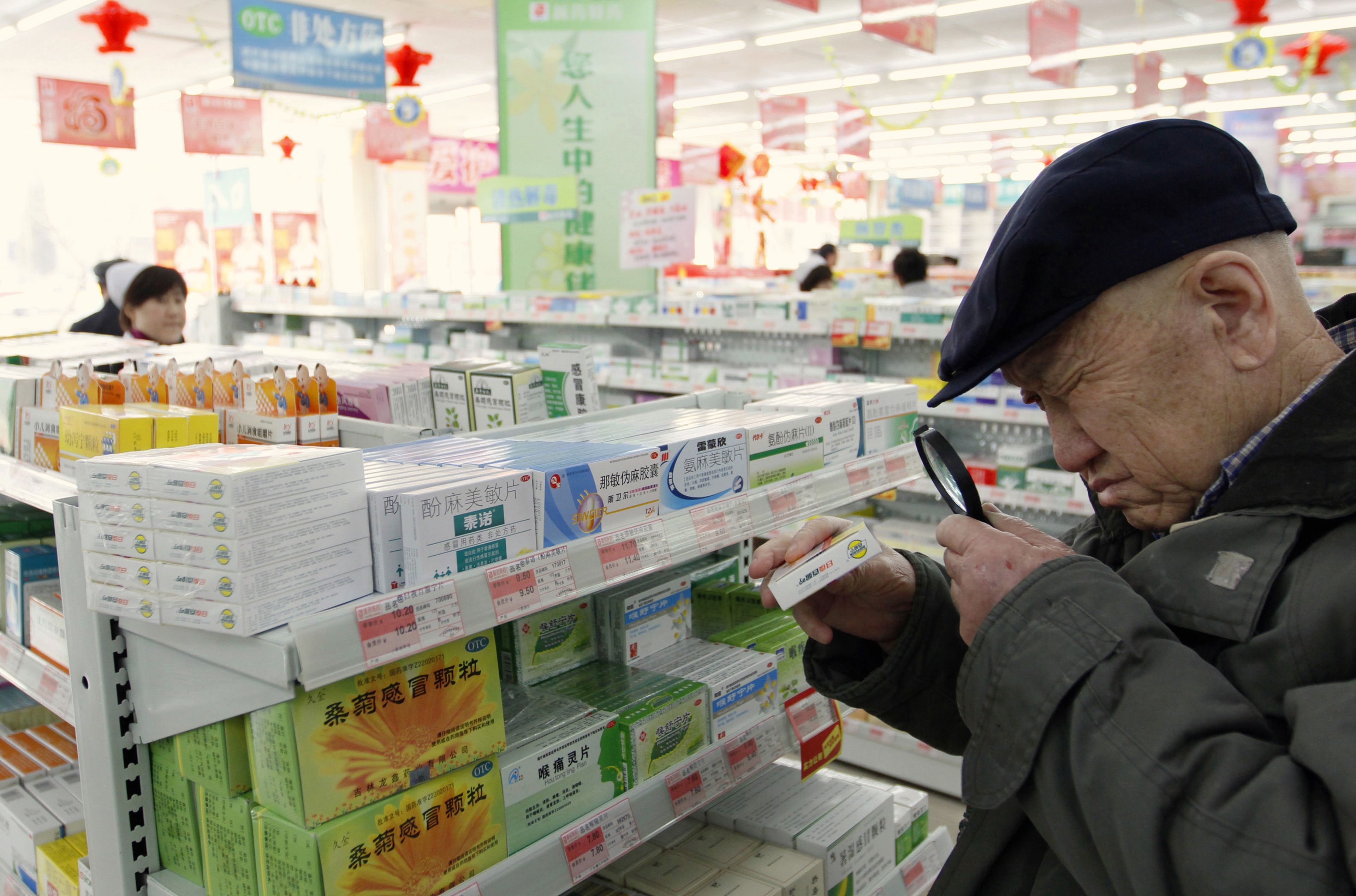 Un hombre mayor mira antibióticos con lupa en una farmacia en China
