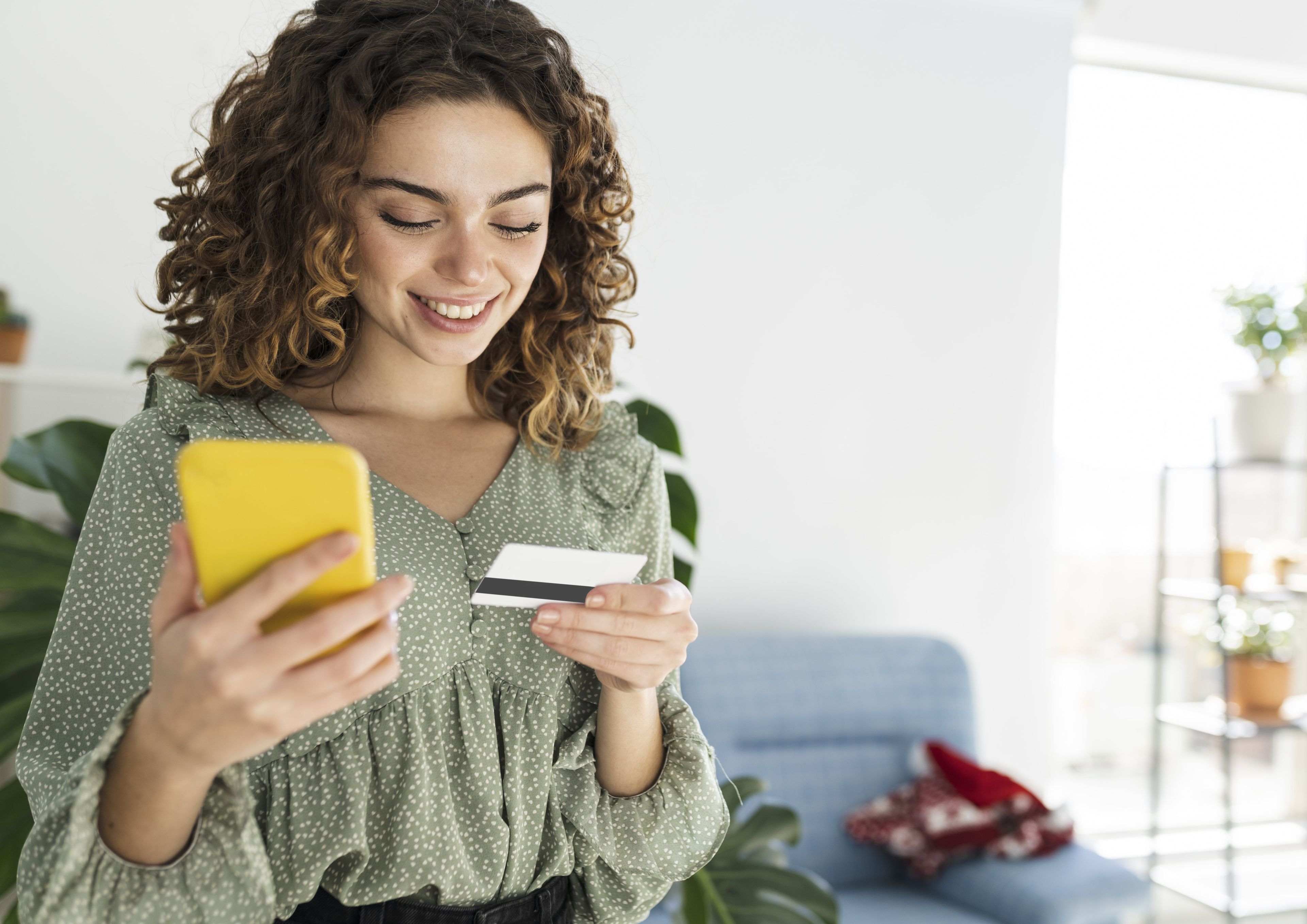 Una mujer joven mira su tarjeta de crédito y el móvil
