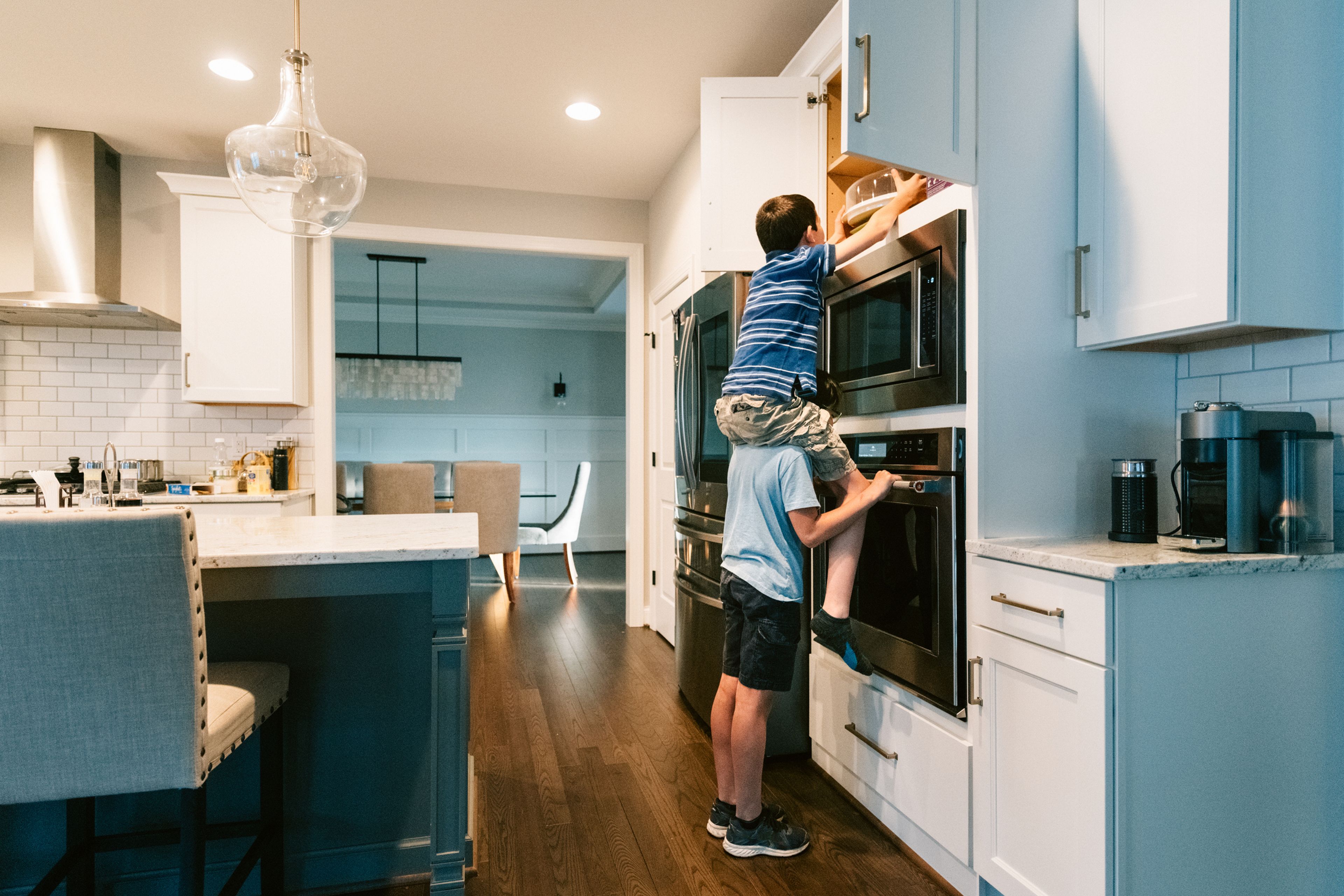 Un niño levanta a otro para coger algo de un mueble de la cocina.